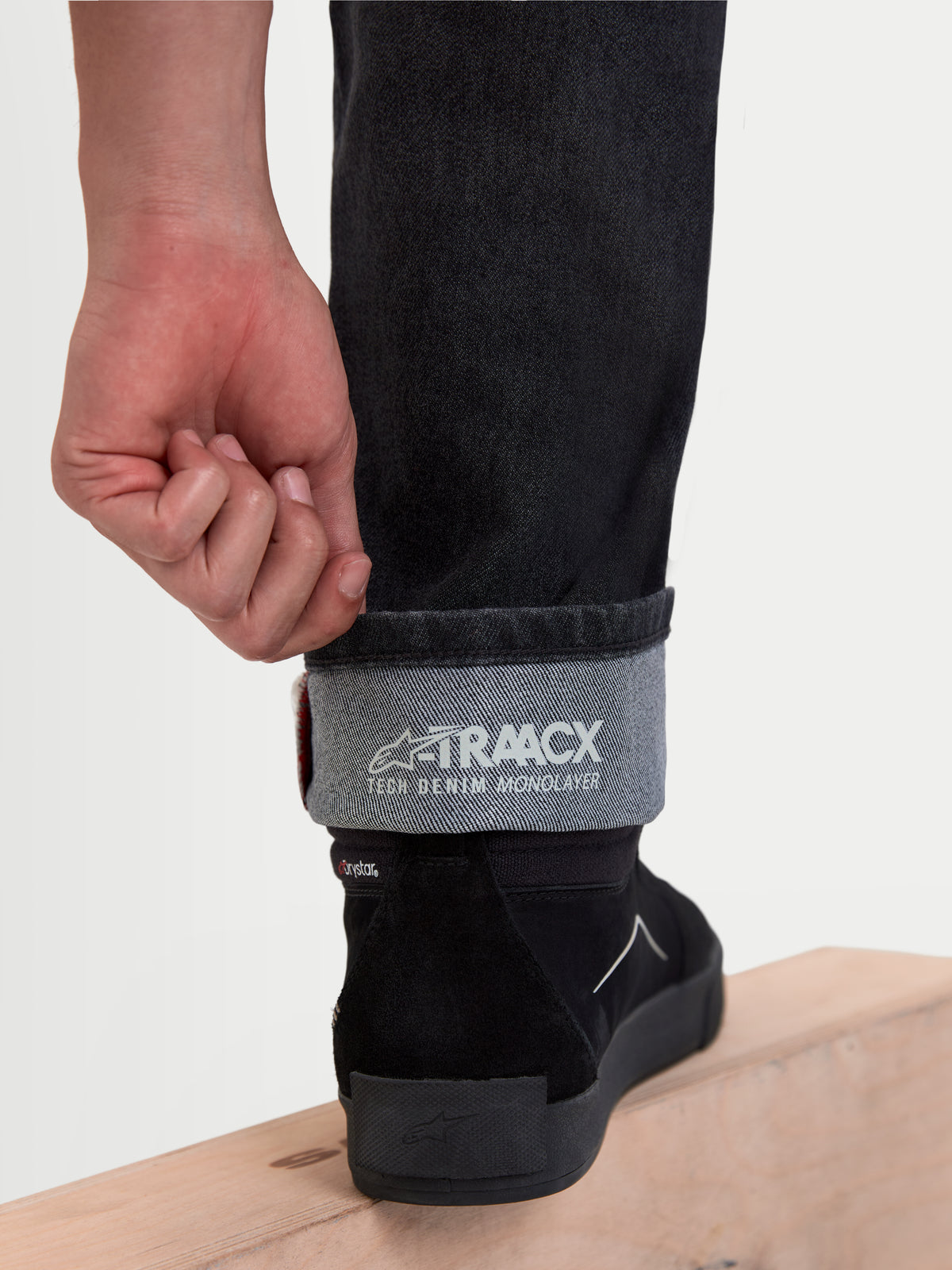 Alpinestars Flex Ast 8 Denim Pantaloni, jeans da moto urbani in nero usato, vista ravvicinata della gamba risvoltata con la struttura in denim tecnico monostrato A-TRAACX e marchio interno