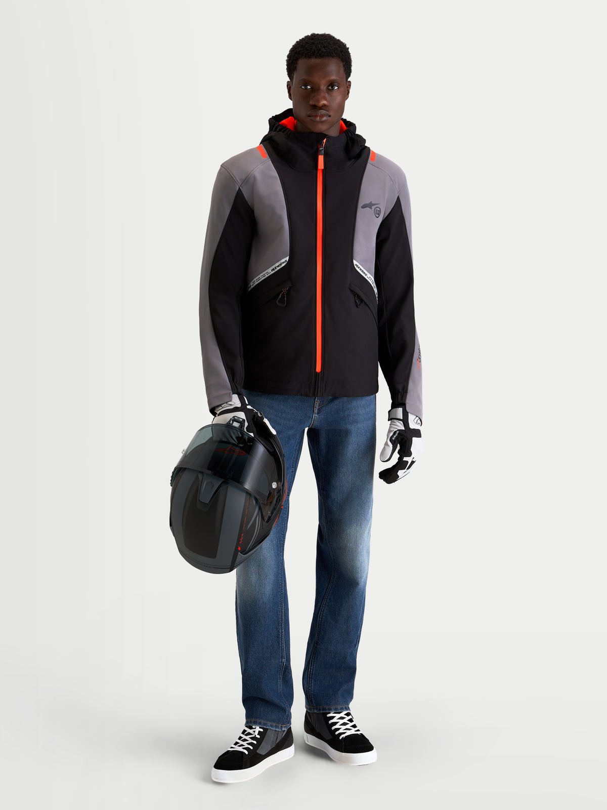 Alpinestars Flex Ast 8 Denim Pantaloni, pantaloni da moto urbani da uomo in blu medio, indossati da un modello che tiene un casco e indossa una giacca tecnica nera e grigia