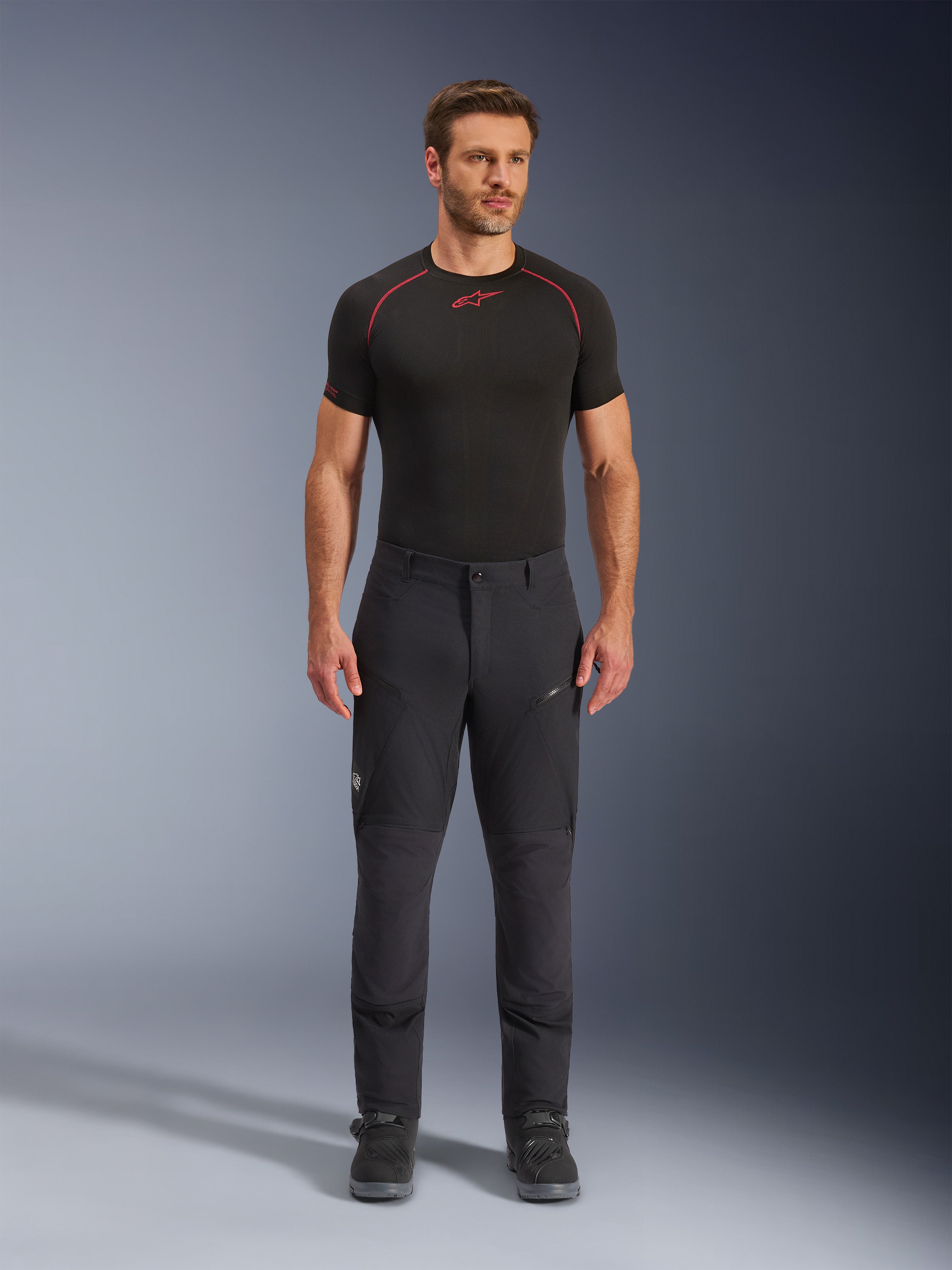 Alpinestars Flex-AST Explorer Pants, pantaloni da moto adventure touring neri, uomo che indossa pantaloni tecnici aderenti con tasche cargo con zip e pannelli rinforzati, abbinati a base layer nero e stivali da moto, protezione resistente per la guida adventure