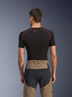 Alpinestars Flex-AST Explorer Pants, vista posteriore su modello, colore Walnut Black, caratterizzati da tessuto marrone con pannelli rinforzati neri sulla seduta e vita elasticizzata, abbinati a un base layer nero a maniche corte con cuciture rosse.