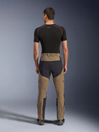 Pantaloni Alpinestars Flex-AST Explorer, Walnut Black, vista posteriore su modello, con seduta nera rinforzata e tessuto elasticizzato marrone, abbinati a base layer nero e stivali tecnici da moto, abbigliamento resistente per adventure riding