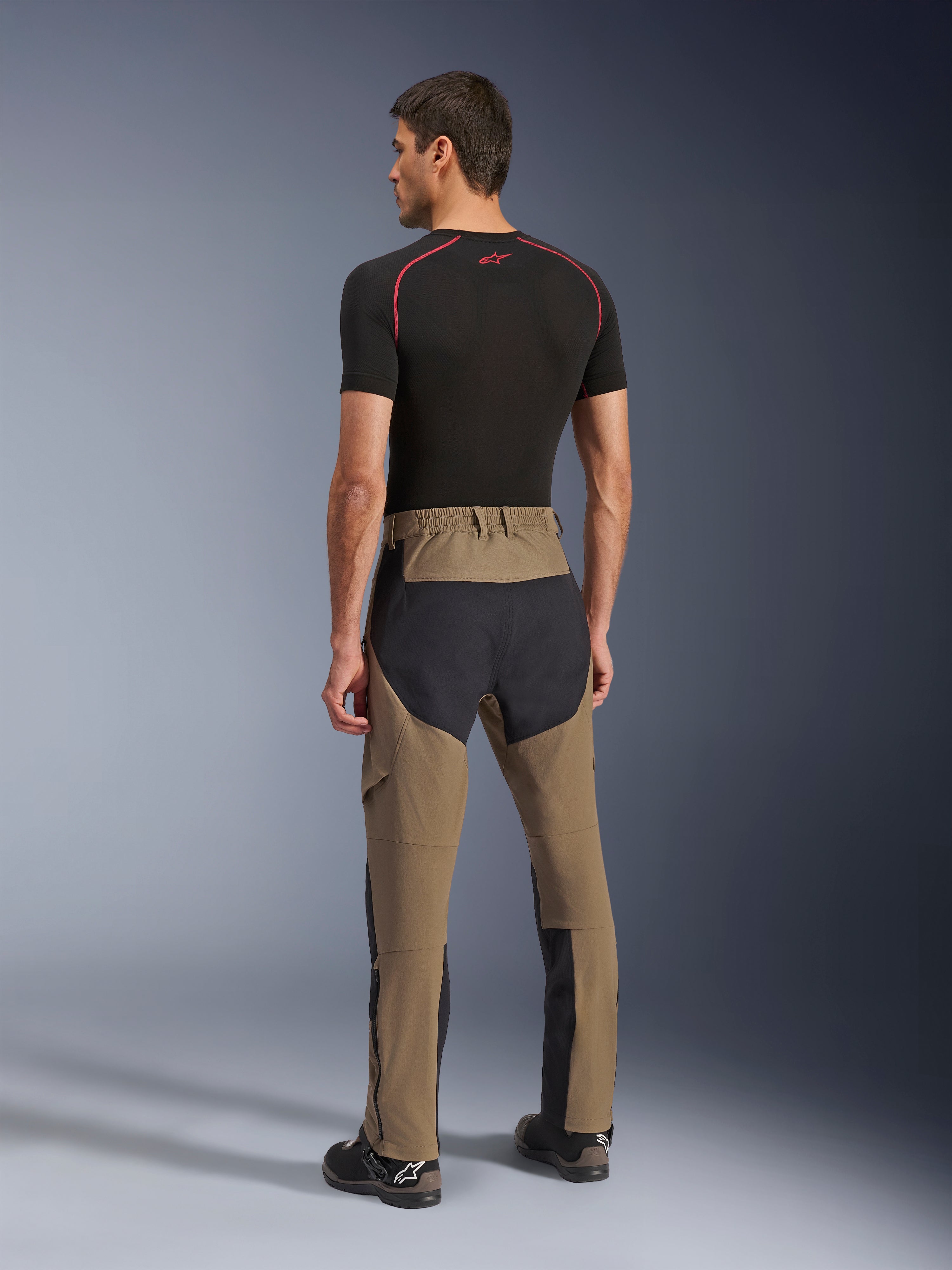 Pantaloni Alpinestars Flex-AST Explorer, pantaloni da moto adventure, Walnut Black, vista posteriore su modello con pannelli neri in ripstop su seduta e gambe, costruzione in tessuto elasticizzato e lunghe cerniere a fondo gamba per l'adventure touring