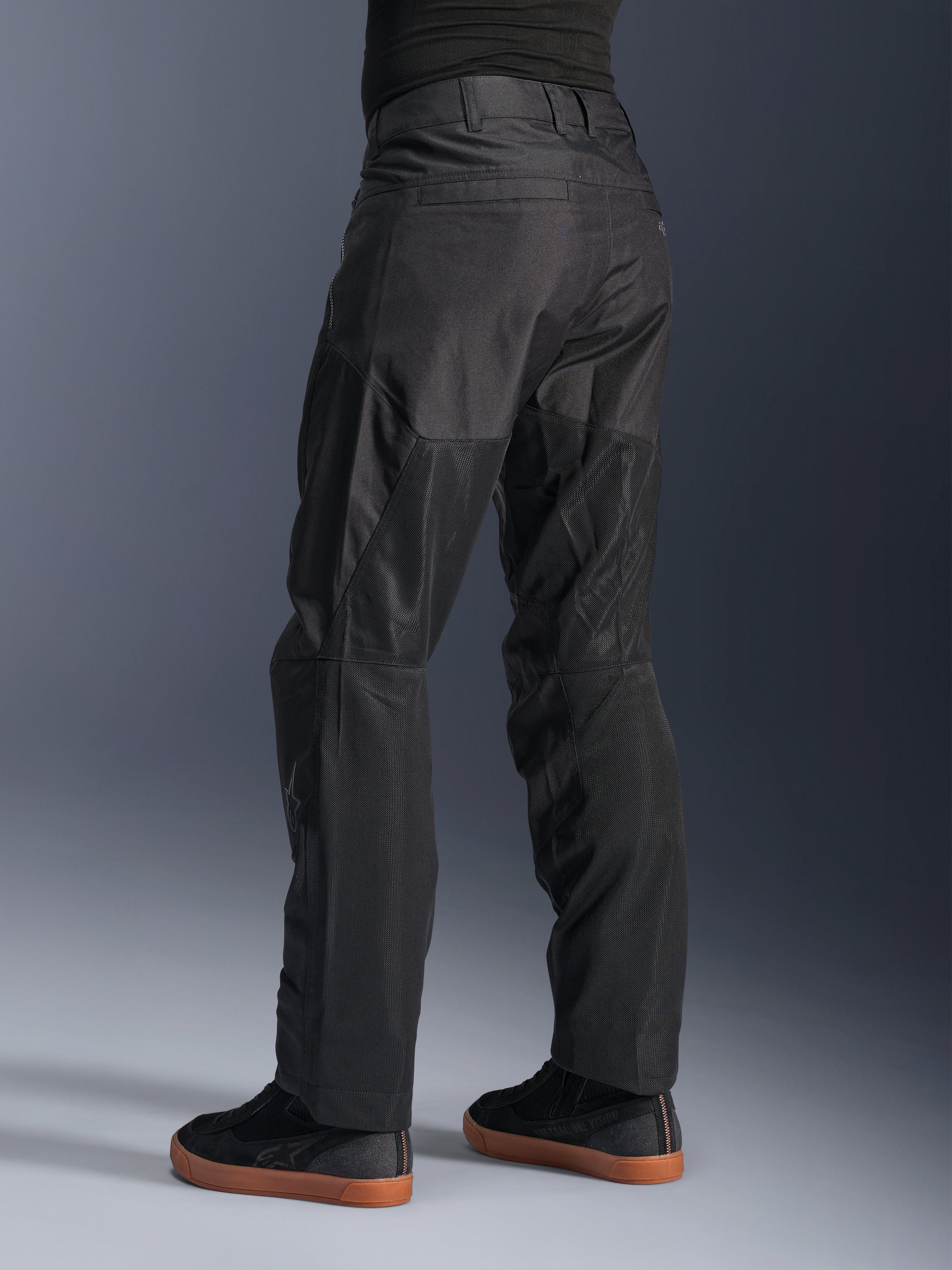 Alpinestars C-1 Air Pants, pantaloni da moto urban, nero, vista posteriore che mostra ampi pannelli in mesh tecnico sulla parte posteriore delle gambe per la ventilazione, design pulito per la guida in città, indossati con sneaker casual nere.