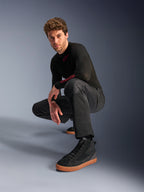Alpinestars C-1 Air Pants, pantaloni da moto urban, nero, modello accovacciato in studio, indossati con maglia nera a maniche lunghe e sneakers nere con suole marroni, dotati di pannelli in mesh traspirante e stile urban contemporaneo