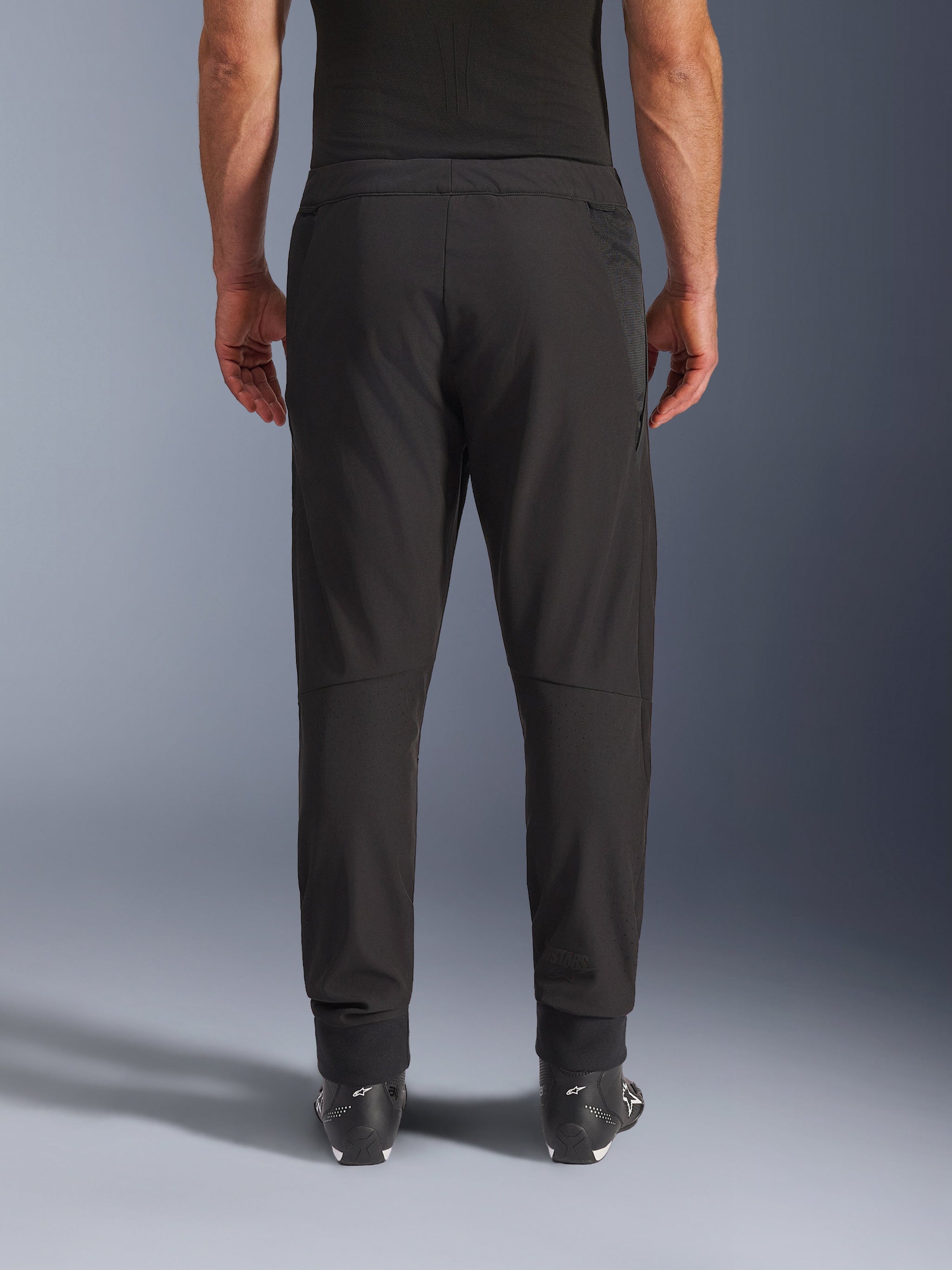Alpinestars Aeroshell Airflow Pants, nero, vista posteriore, con zone traforate al laser sui polpacci e pannelli in mesh, indossati con stivali Alpinestars neri, design softshell leggero per sport e touring