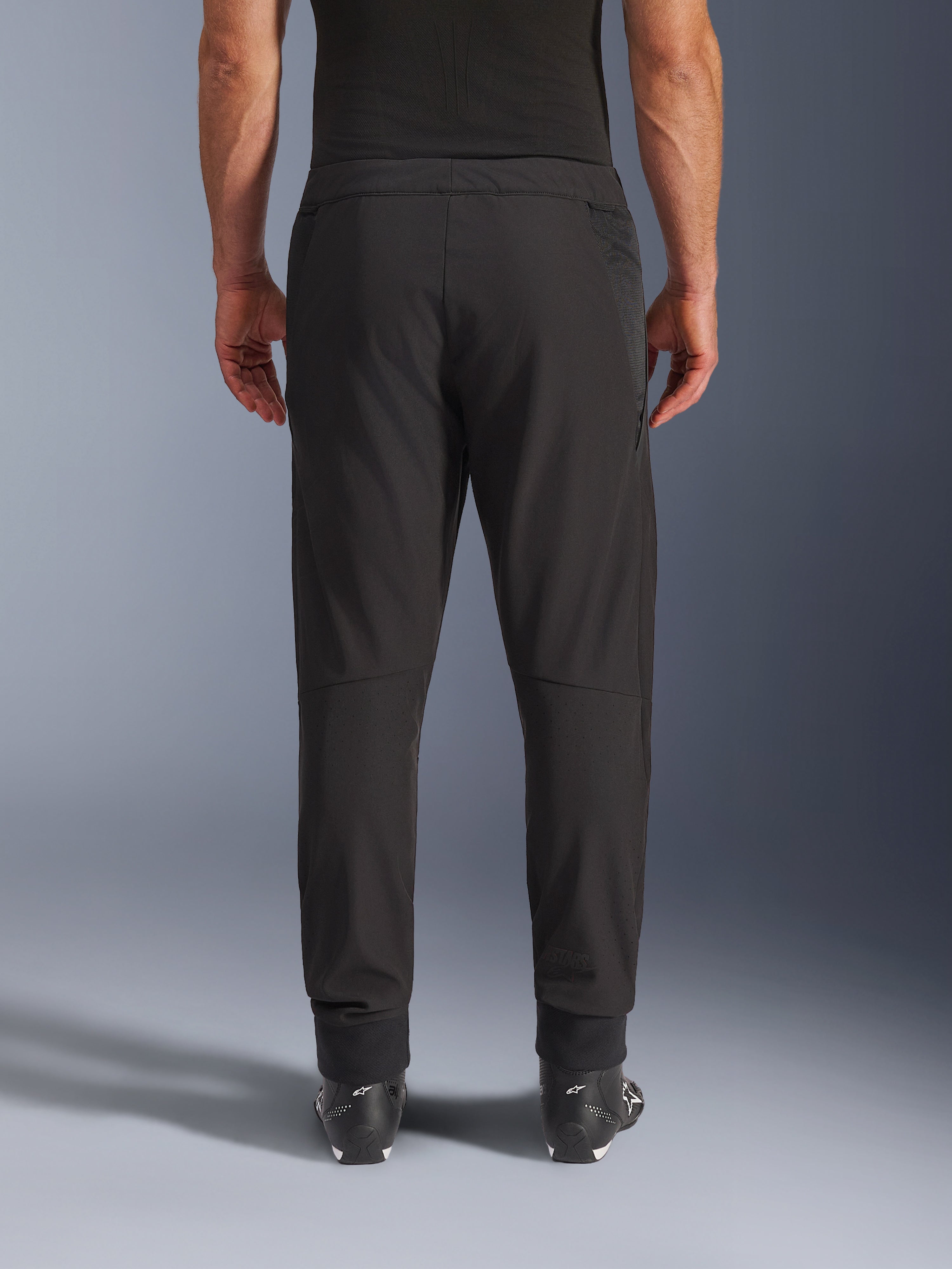Alpinestars Aeroshell Airflow Pants, nero, vista posteriore, con zone traforate al laser sui polpacci e pannelli in mesh, indossati con stivali Alpinestars neri, design softshell leggero per sport e touring