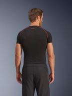 Vista posteriore di un modello che indossa i pantaloni Alpinestars Aeroshell Airflow, neri, costruzione leggera in softshell con pannelli laterali in rete integrati, abbinati a un base layer nero con cuciture rosse a contrasto, abbigliamento sportivo da moto