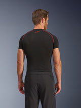 Vista posteriore di un modello che indossa i pantaloni Alpinestars Aeroshell Airflow, neri, costruzione leggera in softshell con pannelli laterali in rete integrati, abbinati a un base layer nero con cuciture rosse a contrasto, abbigliamento sportivo da moto