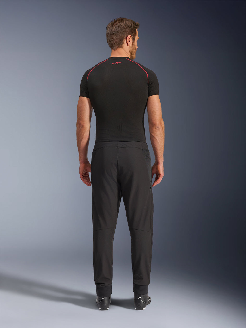 Alpinestars Aeroshell Airflow Pants, pantaloni da moto neri, vista posteriore mostrata su un modello con base layer nero e stivali, con telaio softshell leggero e pannelli in rete integrati per la ventilazione