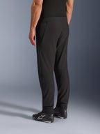Pantaloni Alpinestars Aeroshell Airflow, pantaloni da moto neri, vista posteriore a tre quarti, costruzione in leggero softshell elasticizzato con pannelli in rete integrati, polsini delle caviglie regolabili, indossati con scarpe da moto Alpinestars nere