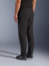 Pantaloni Alpinestars Aeroshell Airflow, pantaloni da moto neri, vista posteriore a tre quarti, costruzione in leggero softshell elasticizzato con pannelli in rete integrati, polsini delle caviglie regolabili, indossati con scarpe da moto Alpinestars nere