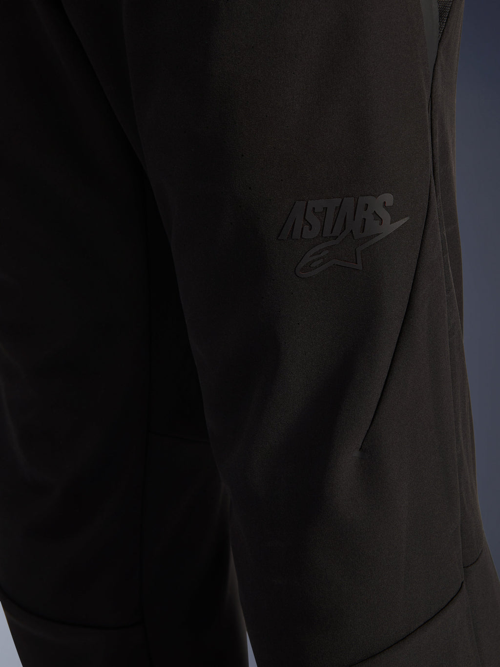 Alpinestars Aeroshell Airflow Pants, pantaloni da moto neri, vista ravvicinata della zona della coscia con logo ASTARS nero a rilievo, materiale softshell elasticizzato leggero con design ergonomico delle cuciture