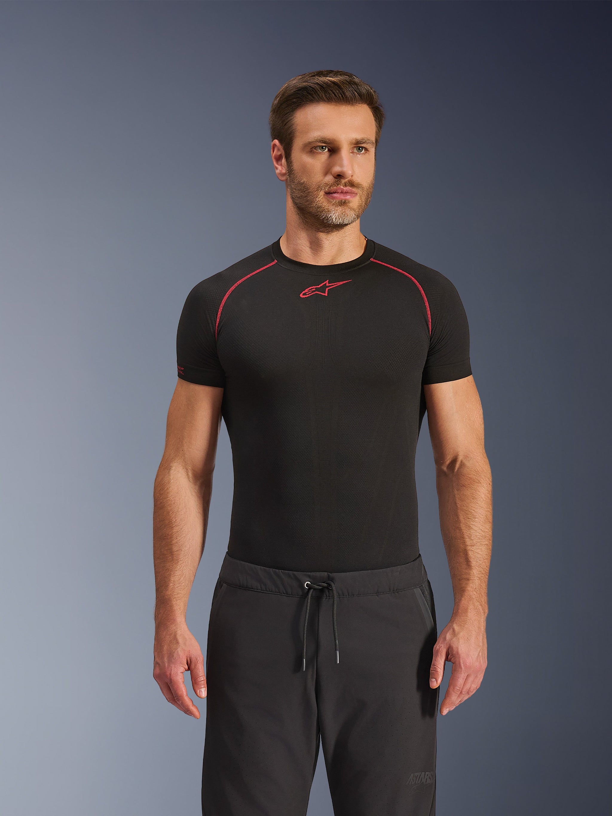 Pantaloni Alpinestars Aeroshell Airflow, pantaloni da moto neri in tessuto softshell leggero, dotati di vita con coulisse e ventilazione traforata al laser, indossati con una maglia base layer Alpinestars nera.