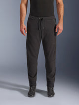 Pantaloni Alpinestars Aeroshell Airflow, pantaloni da moto neri, vista frontale indossati con stivali da moto neri, presentano vita con coulisse e polsini alle caviglie affusolati, design in softshell leggero con branding tonale discreto.