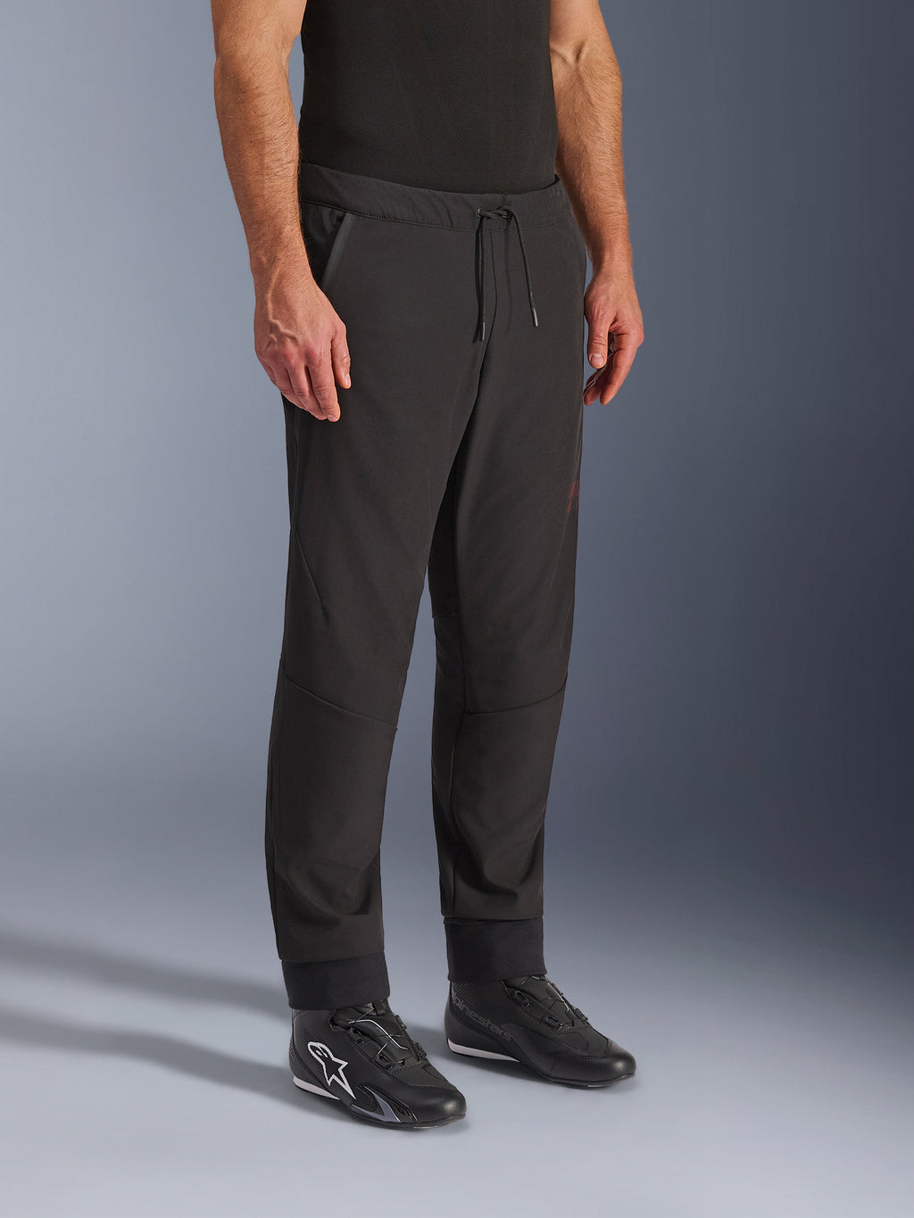 Pantaloni Alpinestars Aeroshell Airflow, pantaloni da moto neri, indossati con scarpe da guida nere, con vita a coulisse, polsini alle caviglie e tessuto softshell perforato al laser per la massima ventilazione