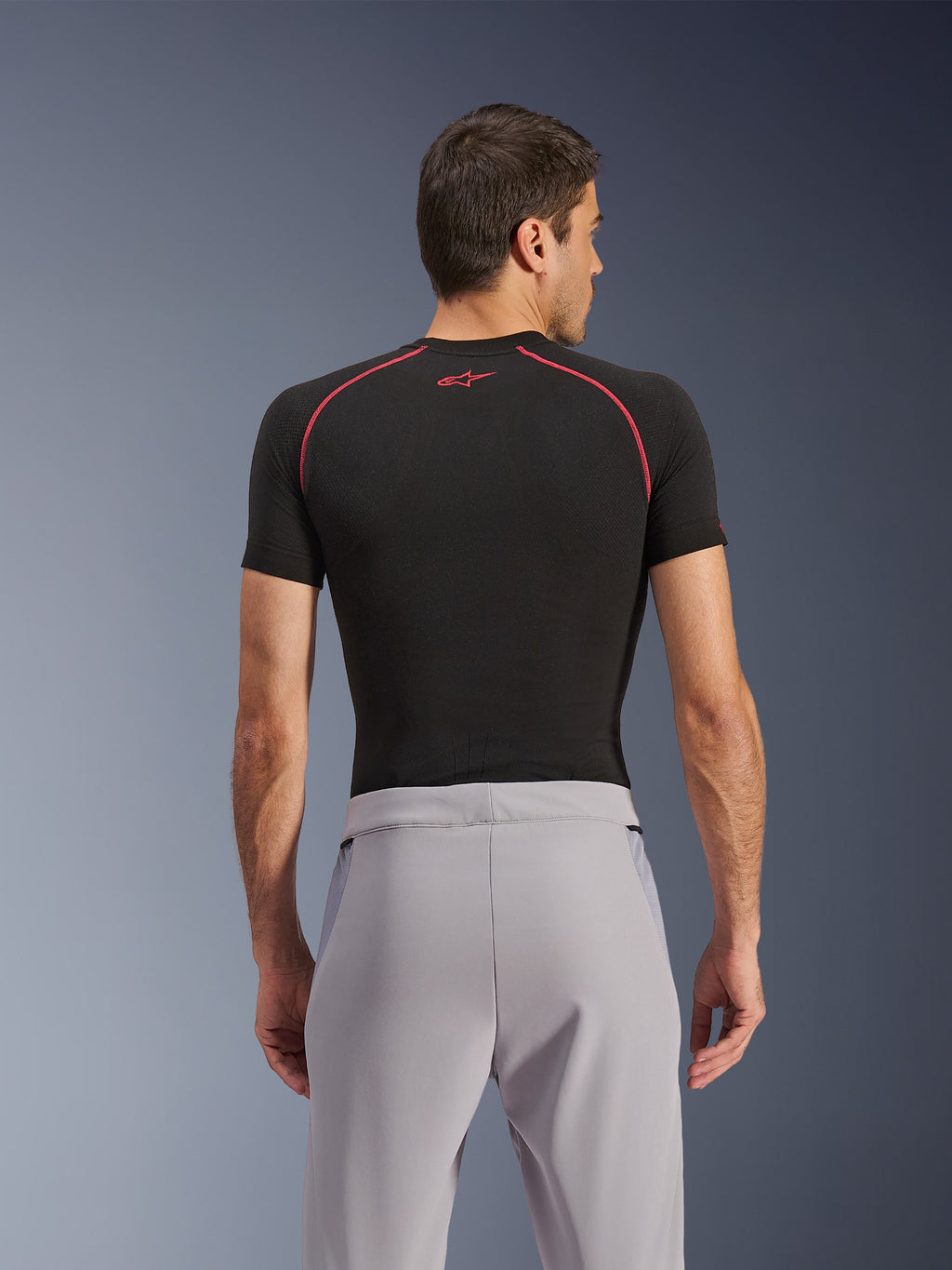 Pantaloni Alpinestars Aeroshell Airflow, Mid Gray, vista posteriore, indossati con un base layer nero a maniche corte con cuciture e logo rossi, caratterizzati da tessuto softshell elastico leggero e pannelli in rete per la massima ventilazione, vestibilità sportiva ergonomica per la guida della moto