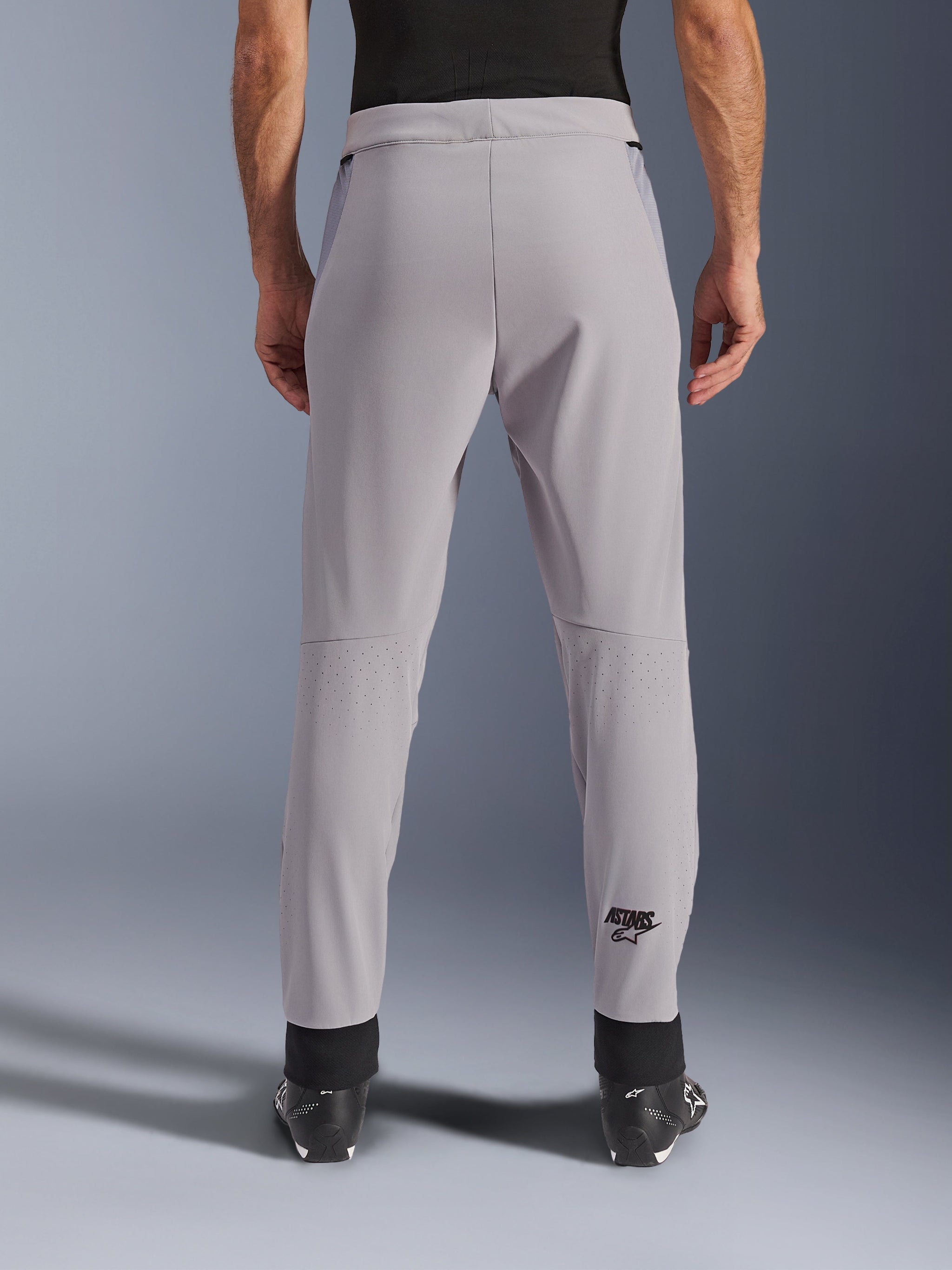 Pantaloni Alpinestars Aeroshell Airflow, pantaloni da moto, grigio medio, vista posteriore con zone traforate al laser sui polpacci e logo Astars nero, costruzione in softshell con polsini neri alle caviglie e pannelli in mesh sui fianchi.
