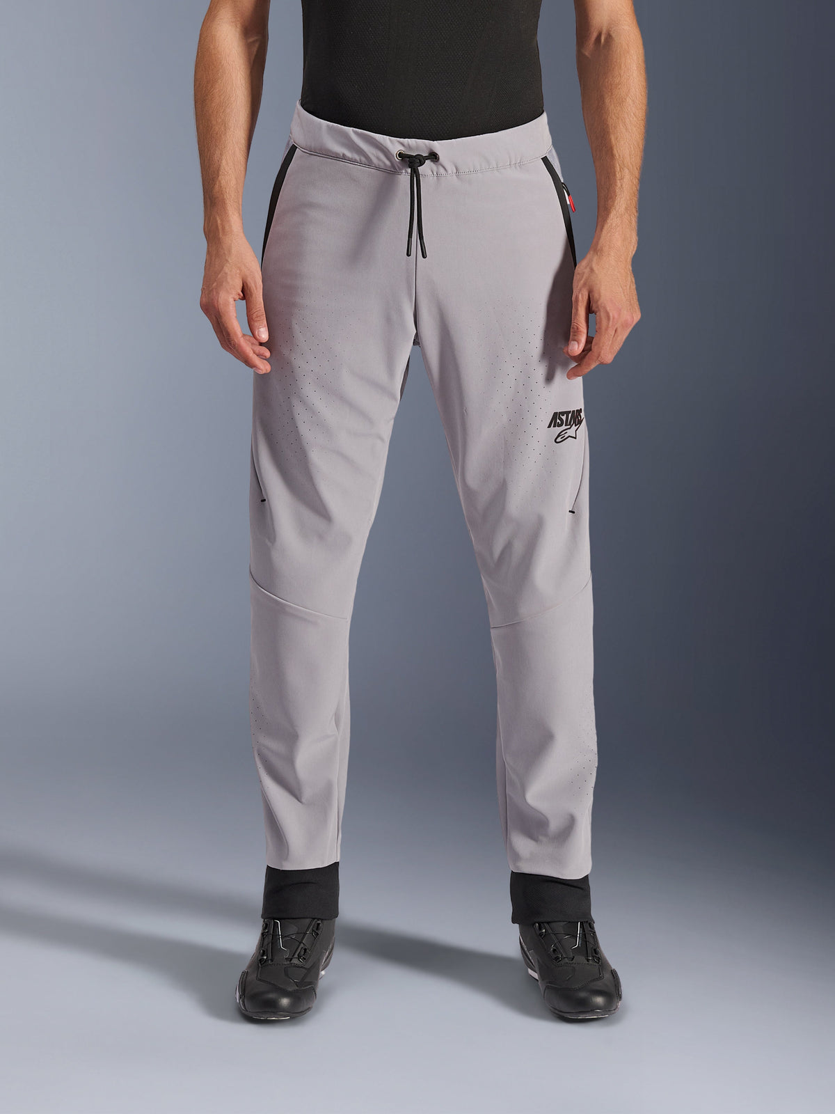 Pantaloni Alpinestars Aeroshell Airflow, grigio medio, vista frontale che mostra zone traforate al laser su cosce e stinchi, vita con cordino nero e logo ASTARS nero, struttura in softshell leggero per la guida in climi caldi