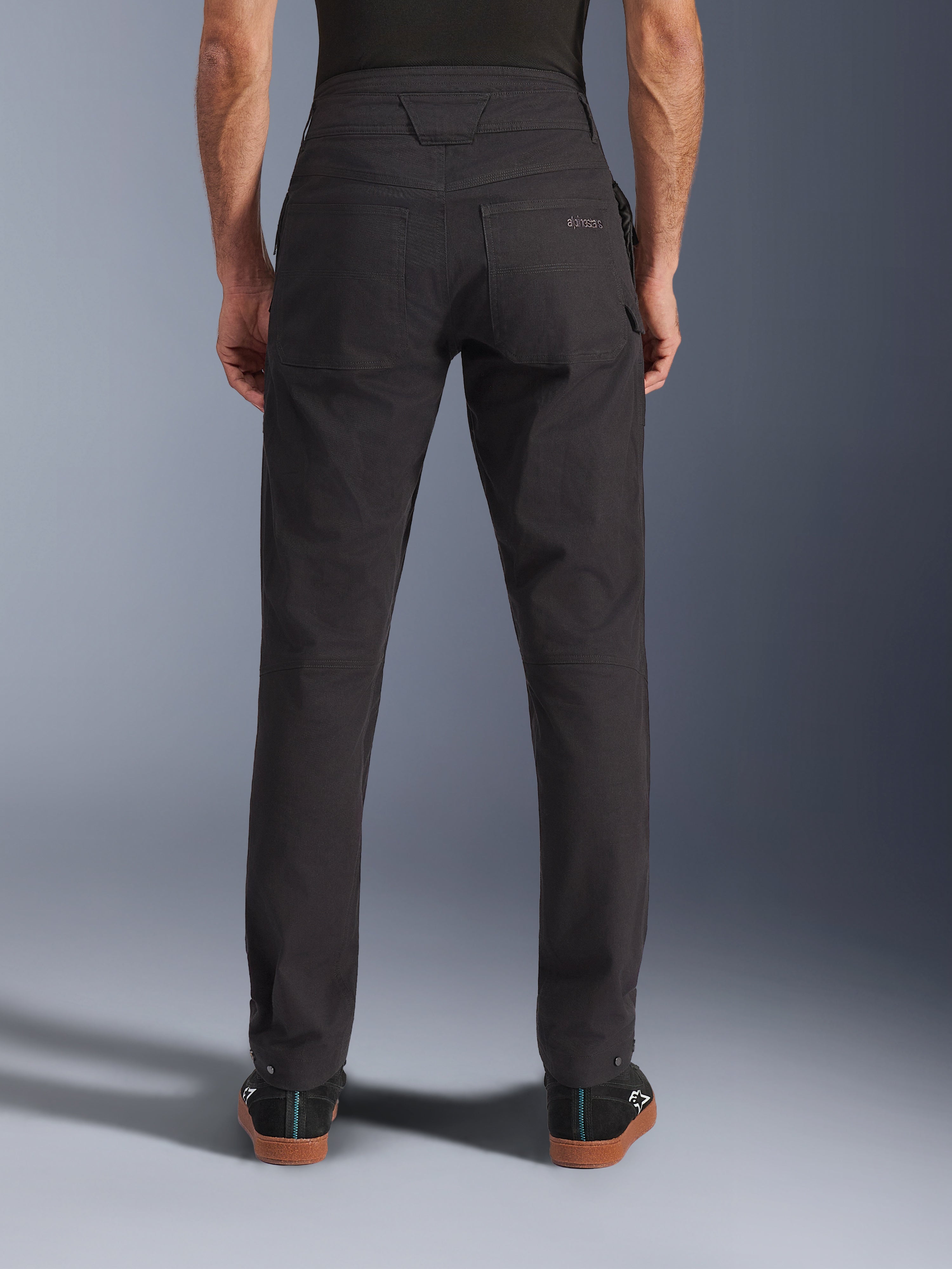 Alpinestars Flex-AST Canvas Pants, pantaloni da moto urban, nero, vista posteriore con tasche posteriori e logo ricamato, vita posteriore allungata e cuciture ergonomiche, indossati con calzature casual nere