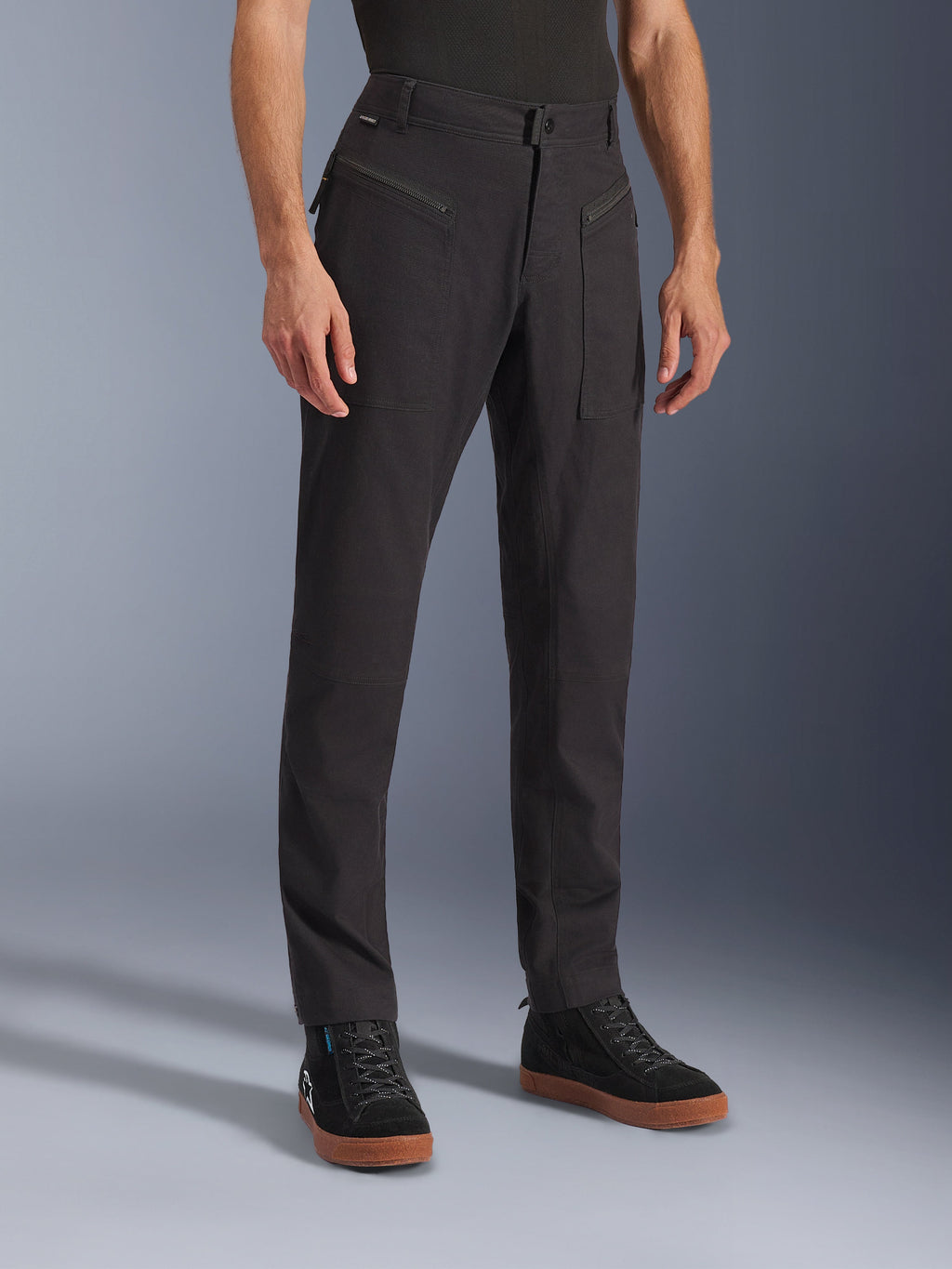 Alpinestars Flex-AST Canvas Pants, pantaloni da moto urbani, nero, indossati da un modello con sneaker nere, caratterizzati da un design workwear heritage, tessuto in twill di policotone elasticizzato e funzionali tasche anteriori con zip.