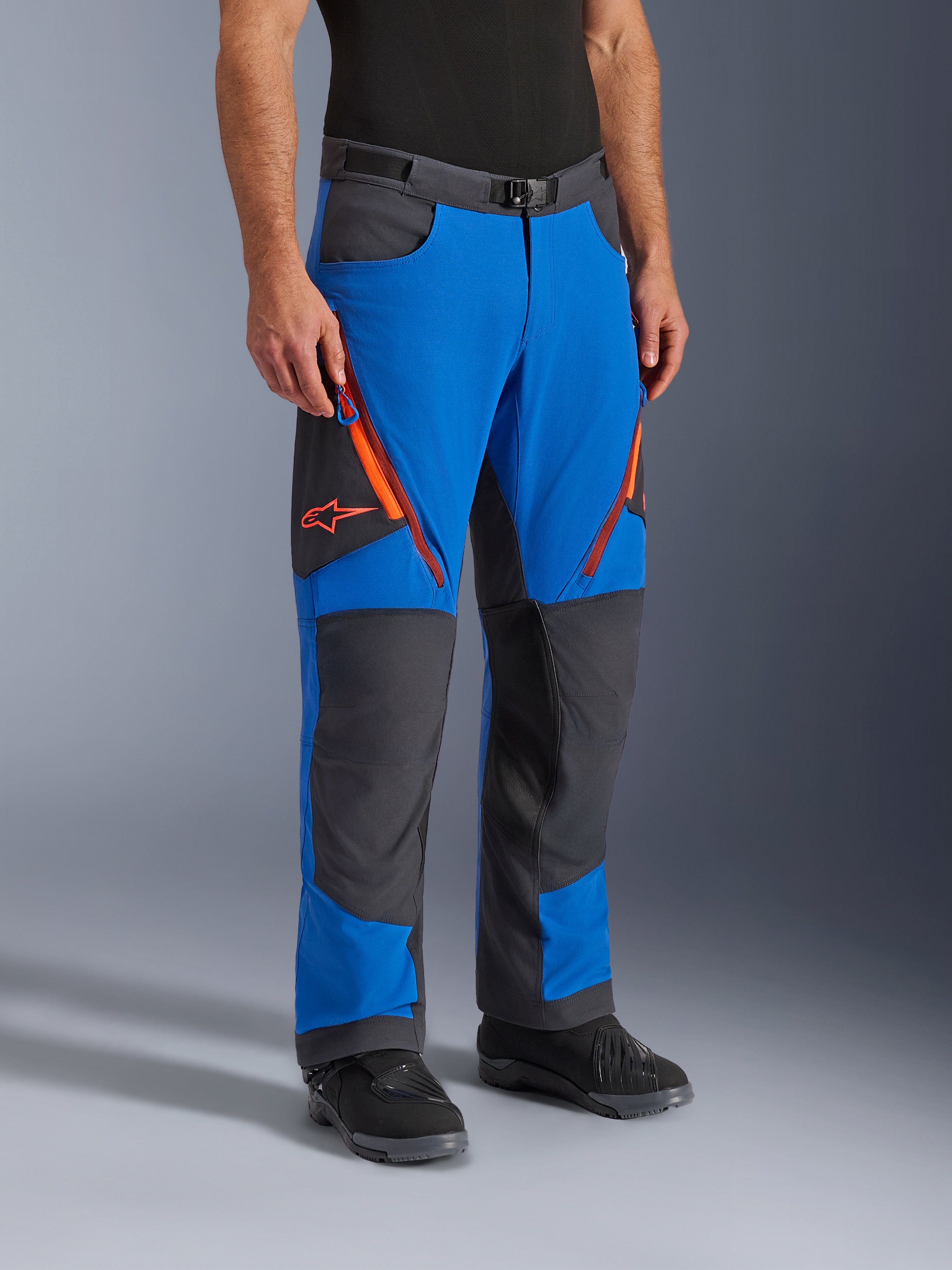 Alpinestars Maxdura Dual Pants, pantaloni da moto adventure, blu reale e grigio scuro con dettagli arancioni, caratterizzati da prese d'aria con zip sulle cosce, pannelli rinforzati sulle ginocchia e cintura con fibbia magnetica, design tecnico sopra-stivale per guida dual-sport.