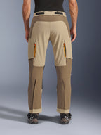 Alpinestars Maxdura Dual Pants, Walnut Aluminum, vista posteriore di pantaloni da moto adventure con pannelli color sabbia e toni della terra, prese d'aria con cerniere arancioni e design sopra lo stivale, indossati con stivali Alpinestars neri