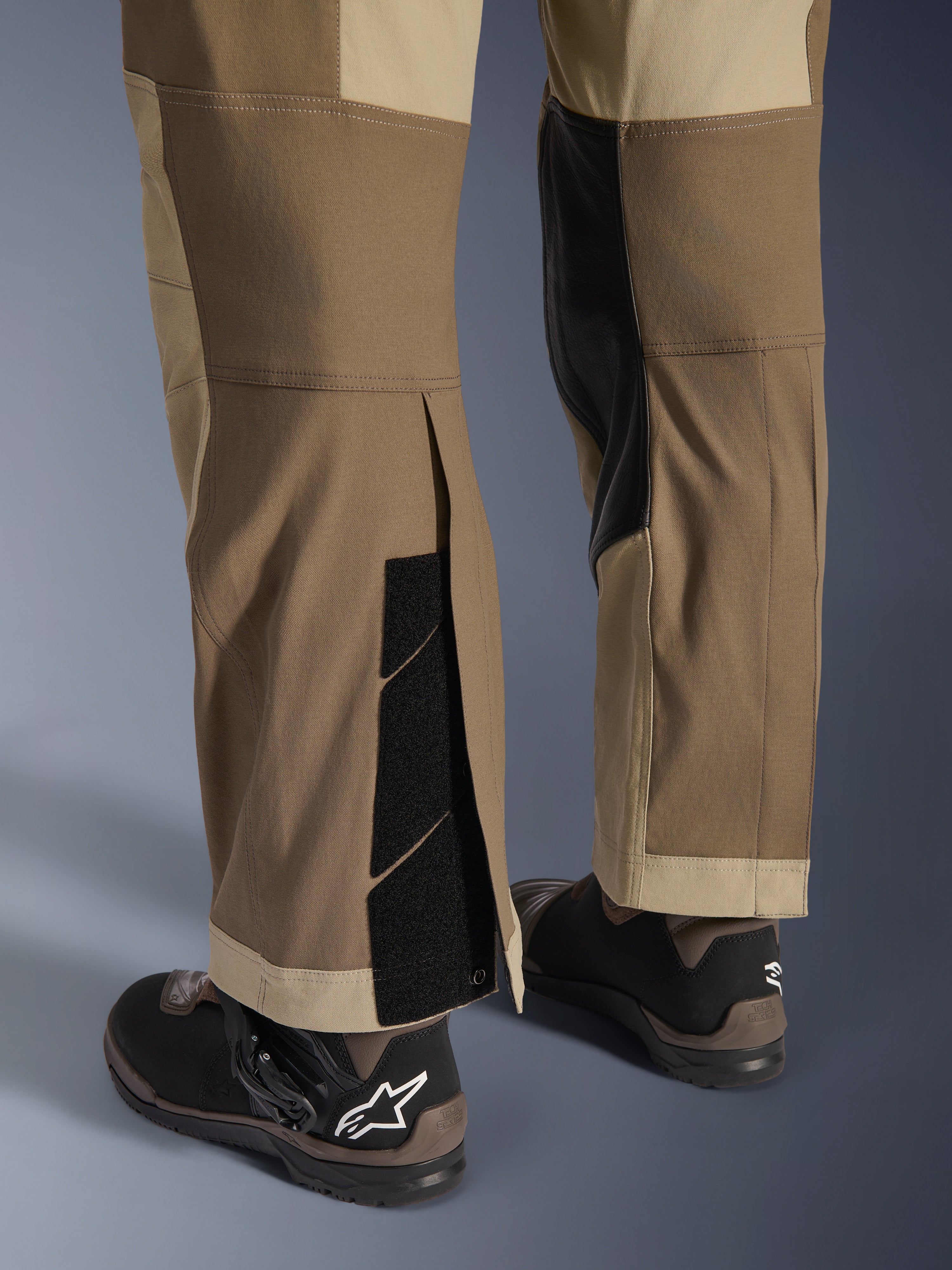 Alpinestars Maxdura Dual Pants in Walnut Aluminum, vista dettagliata della parte inferiore della gamba e dell'orlo con design sopra lo stivale, chiusure a strappo regolabili e pannelli interni rinforzati, abbinati a stivali da moto neri