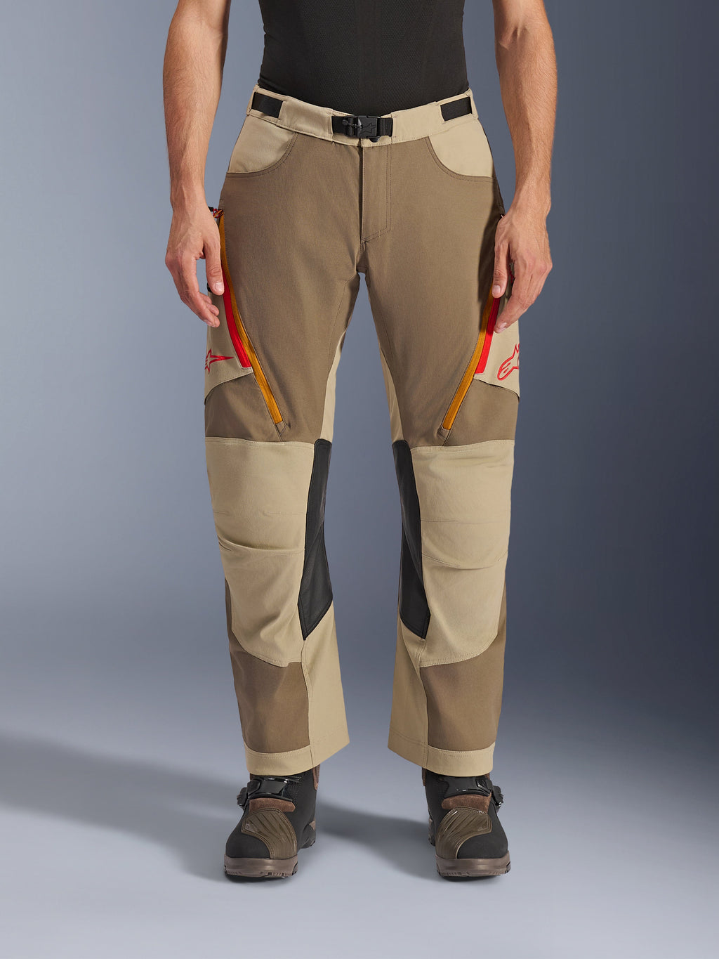 Alpinestars Maxdura Dual Pants, Walnut Aluminum, pantaloni da moto adventure con prese d'aria sulle cosce dotate di zip rosse e arancioni, pannelli interni sulle ginocchia in pelle nera, indossati con un base layer nero e stivali robusti, design multi-tonale resistente per guida dual-sport