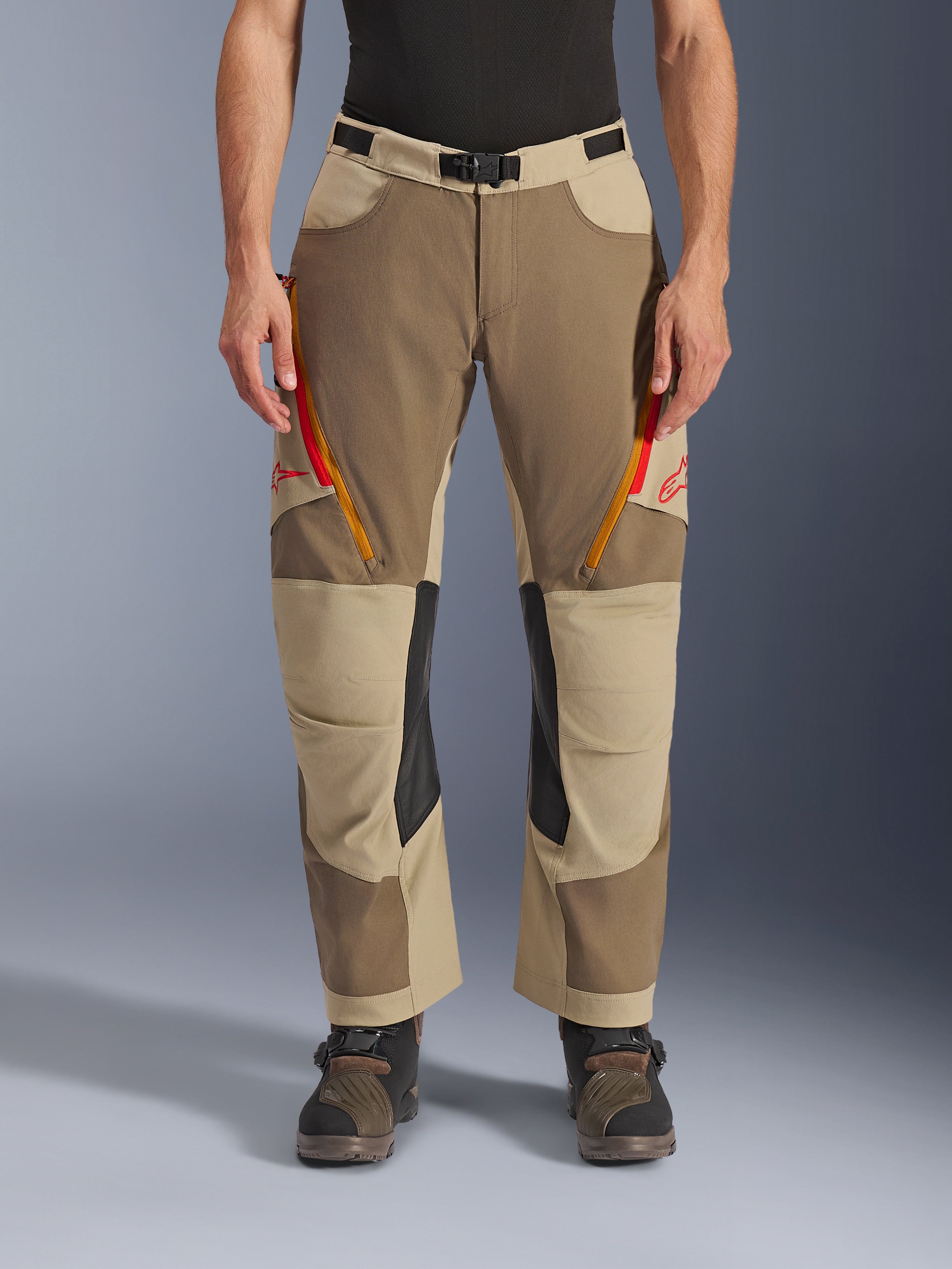 Alpinestars Maxdura Dual Pants, Walnut Aluminum, pantaloni da moto adventure con prese d'aria sulle cosce dotate di zip rosse e arancioni, pannelli interni sulle ginocchia in pelle nera, indossati con un base layer nero e stivali robusti, design multi-tonale resistente per guida dual-sport
