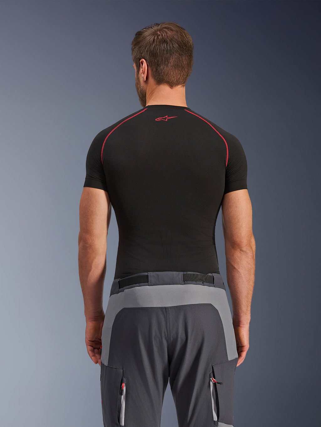 Pantaloni Alpinestars Maxdura Dual, pantaloni da moto adventure, grigio scuro e grigio intenso, vista posteriore con pannelli rinforzati su seduta e vita, indossati con un base layer nero a maniche corte, tasche con cerniera e dettagli rossi