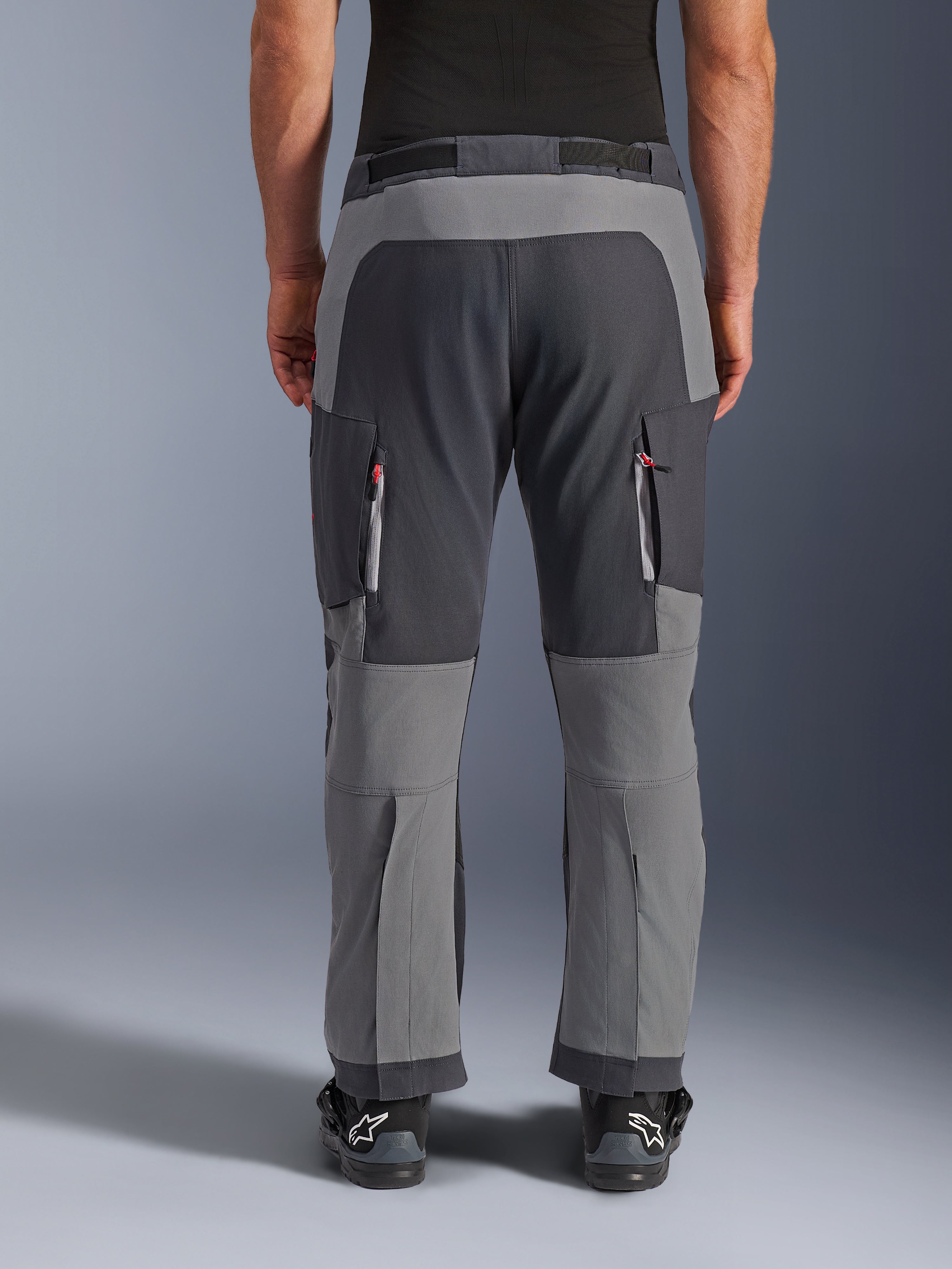 Alpinestars pantaloni Maxdura Dual, pantaloni da moto adventure, grigio scuro e grigio intenso, vista posteriore con pannelli rinforzati su seduta e ginocchia, prese d'aria con cerniera sulle cosce, indossati con stivali Alpinestars neri, robusta costruzione in poliammide elasticizzata per guida dual-sport.
