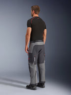 Alpinestars Maxdura Dual Pants, pantaloni da moto adventure, grigio scuro e grigio intenso, indossati da un modello in una vista posteriore laterale, con accenti rossi su cerniere e logo, pannelli grigi rinforzati, tasche cargo e vestibilità over-the-boot