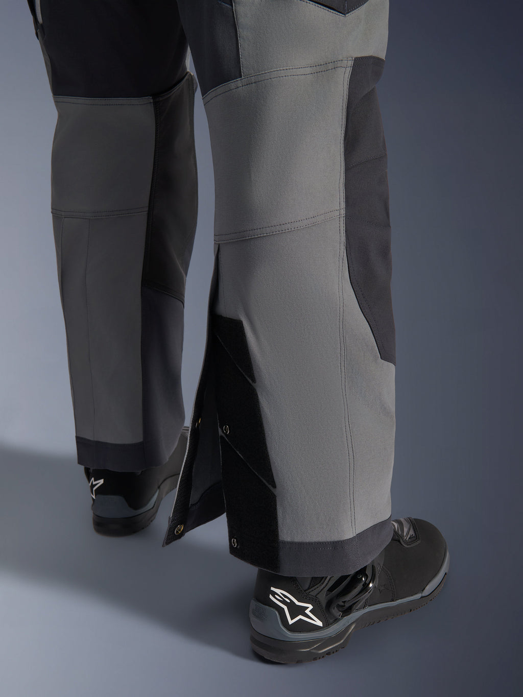 Alpinestars pantaloni Maxdura Dual, pantaloni da moto adventure, grigio scuro e grigio intenso, vista ravvicinata dell'orlo regolabile sopra lo stivale con bottoni a pressione e pannelli rinforzati, indossati con stivali Alpinestars neri, design tecnico robusto per guida dual-sport