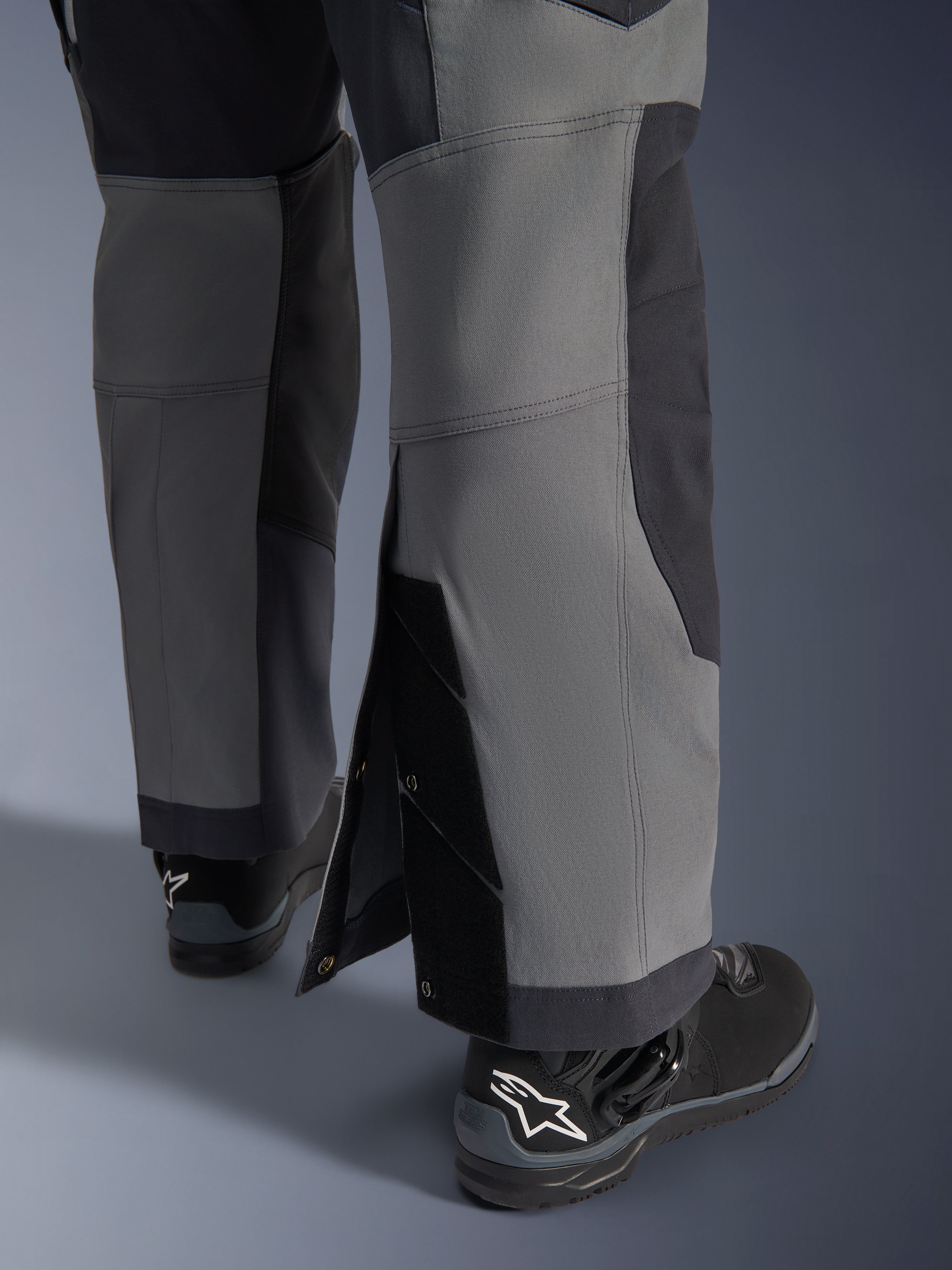 Alpinestars pantaloni Maxdura Dual, pantaloni da moto adventure, grigio scuro e grigio intenso, vista ravvicinata dell'orlo regolabile sopra lo stivale con bottoni a pressione e pannelli rinforzati, indossati con stivali Alpinestars neri, design tecnico robusto per guida dual-sport