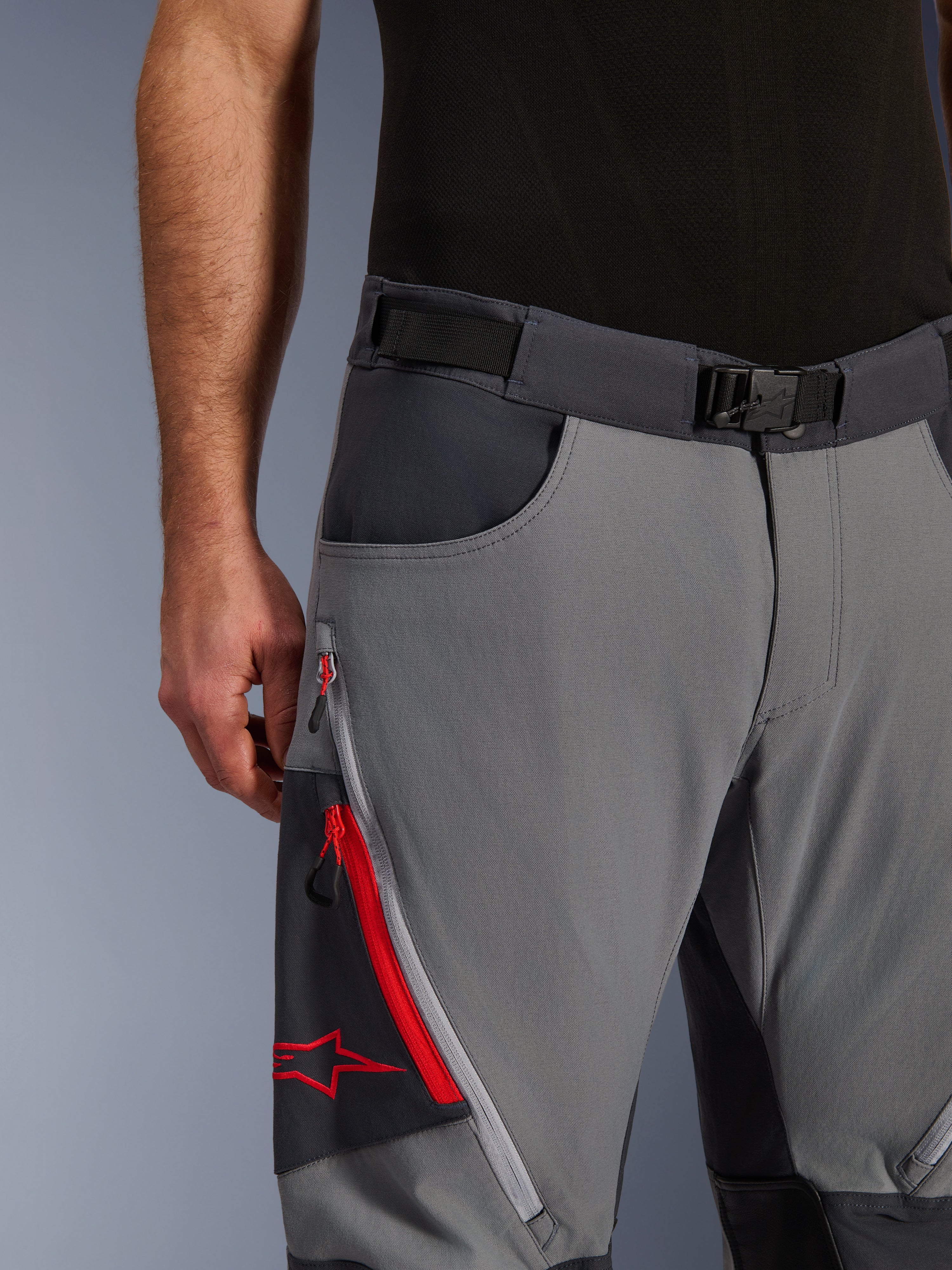 Alpinestars Maxdura Dual Pants, pantaloni da moto adventure, grigio scuro e grigio intenso, primo piano con cintura regolabile con fibbia magnetica, tasca cargo con zip con dettagli rossi e logo Alpinestars.