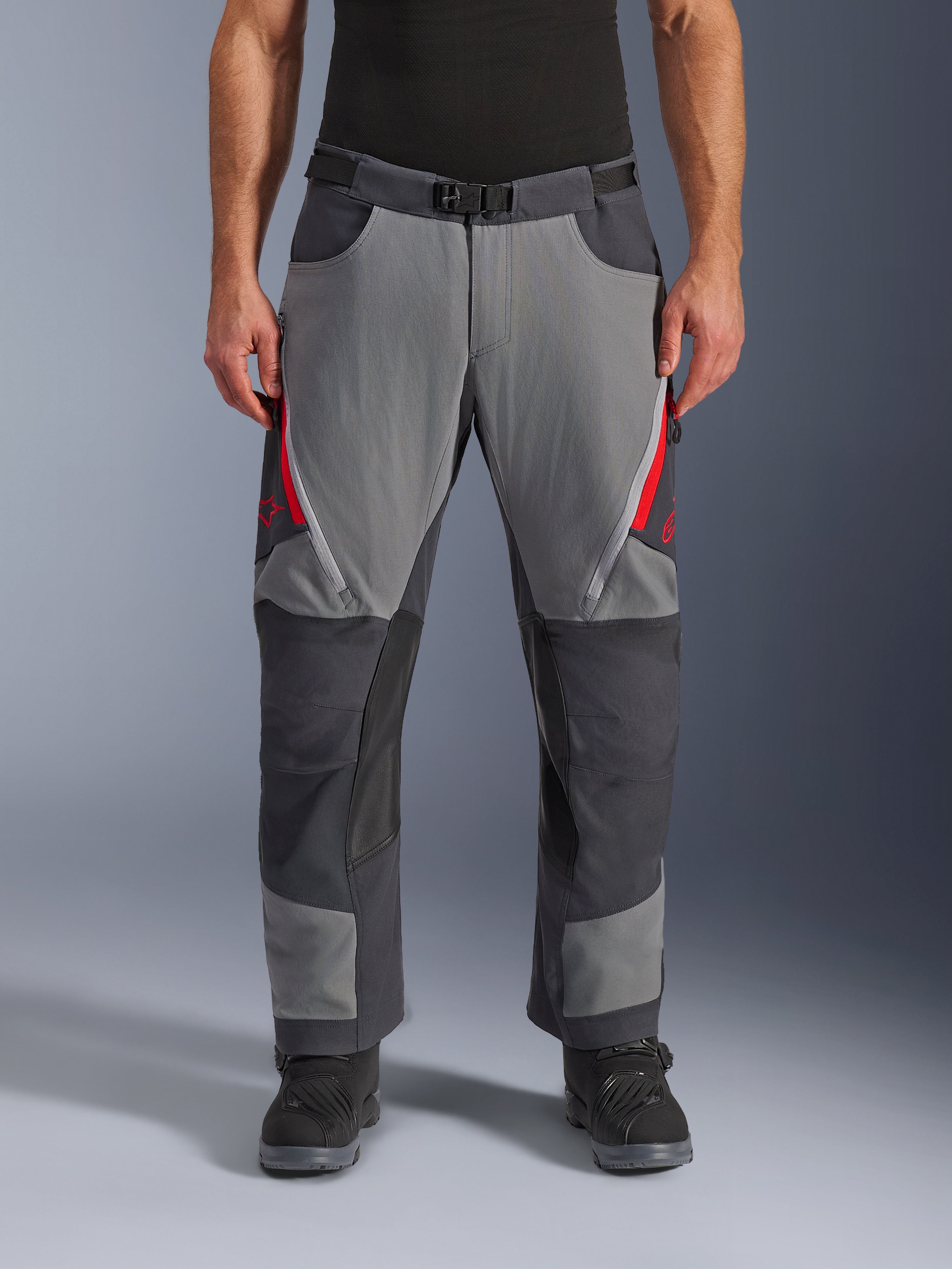 Pantaloni Alpinestars Maxdura Dual, pantaloni da moto adventure, grigio scuro e grigio intenso con accenti rossi, vista frontale che mostra le prese d'aria con cerniera sulle cosce, cintura con fibbia magnetica e pannelli rinforzati sulle ginocchia, design over-boot per guida dual-sport.