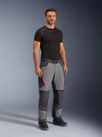 Alpinestars Maxdura Dual Pants, pantaloni da moto adventure, grigio scuro e grigio intenso, indossati con base layer nero e stivali, con prese d'aria rosse con zip, pannelli rinforzati su ginocchia e seduta, vita con cintura, vestibilità atletica per guida dual-sport