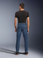 Uomo visto di spalle che indossa pantaloni Alpinestars Flex-AST 5 Denim in Indigo Washed, jeans da moto urbani con vestibilità affusolata moderna e tasche posteriori, abbinati a un base layer nero a maniche corte e scarpe casual nere.