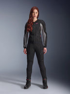 Giacca e pantaloni Alpinestars Stella Troop-Air, completo da moto per donna, nero con dettagli Ash Gray e Pink Fluo, indossati da una modella con capelli rossi, con ventilazione in mesh e design protettivo, posa in studio.