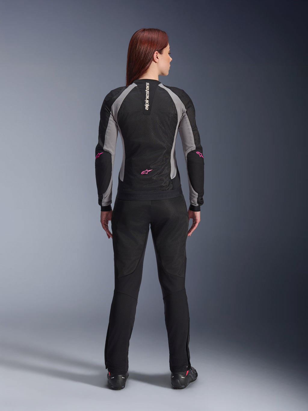 Alpinestars Stella Troop-Air Pants da donna in nero, vista posteriore, abbinati a una giacca da moto in mesh nera e grigia con accenti rosa, scatto in studio che mostra il design tecnico in tessuto ventilato.