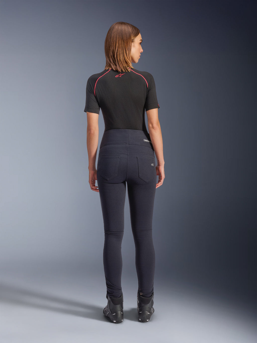 Alpinestars Stella Flex-AST Leggings in nero, pantaloni da moto da donna a vita alta, vista posteriore che mostra la vestibilità skinny e le tasche posteriori, indossati con top nero a maniche corte e stivali da moto, abbigliamento per guida urbana