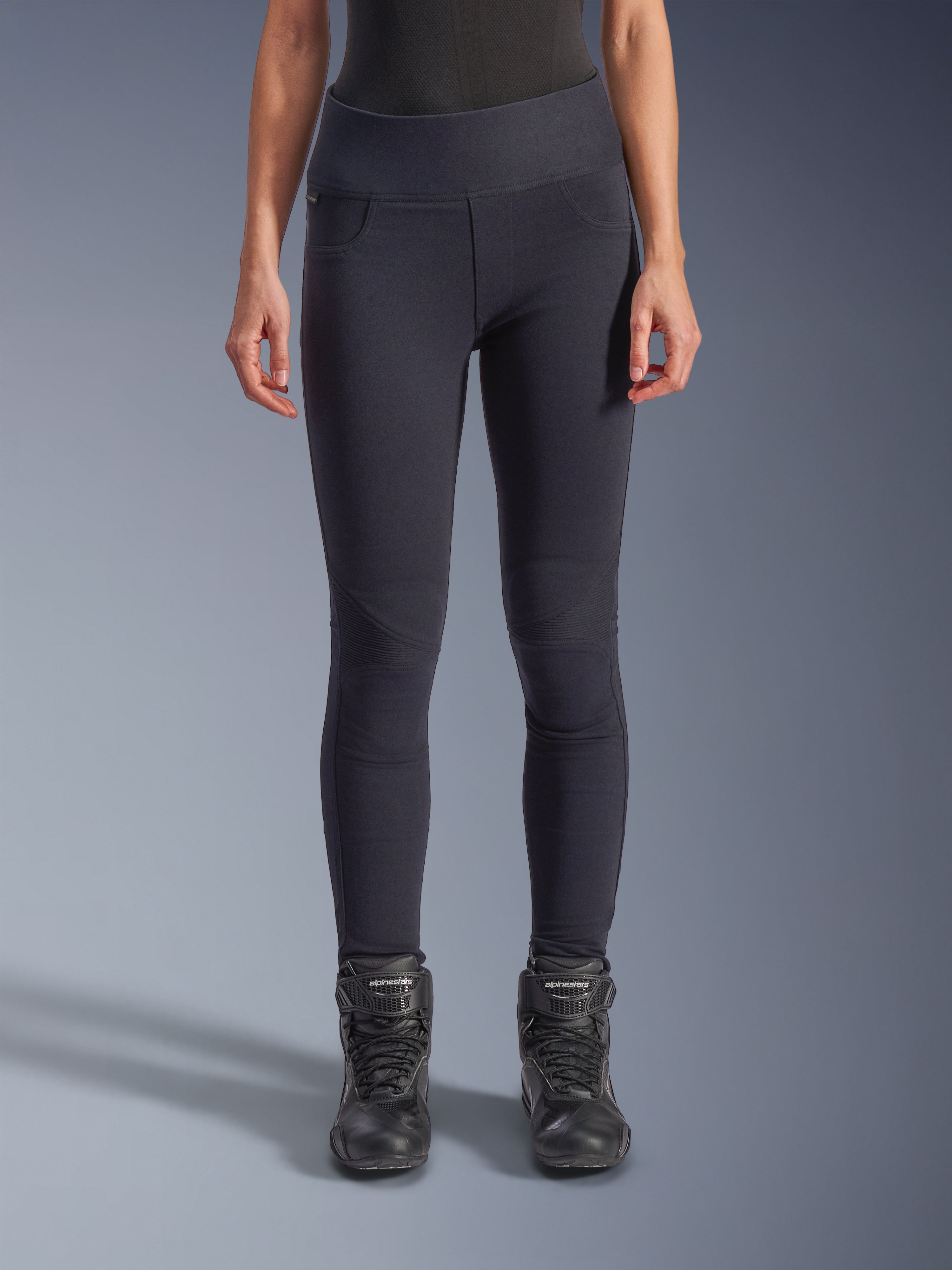Alpinestars Stella Flex-Ast Leggings, leggings da moto da donna, neri, vestibilità a vita alta con pannelli articolati sulle ginocchia e cuciture sagomate, indossati da una modella con stivali da moto neri, abbigliamento tecnico urban performance