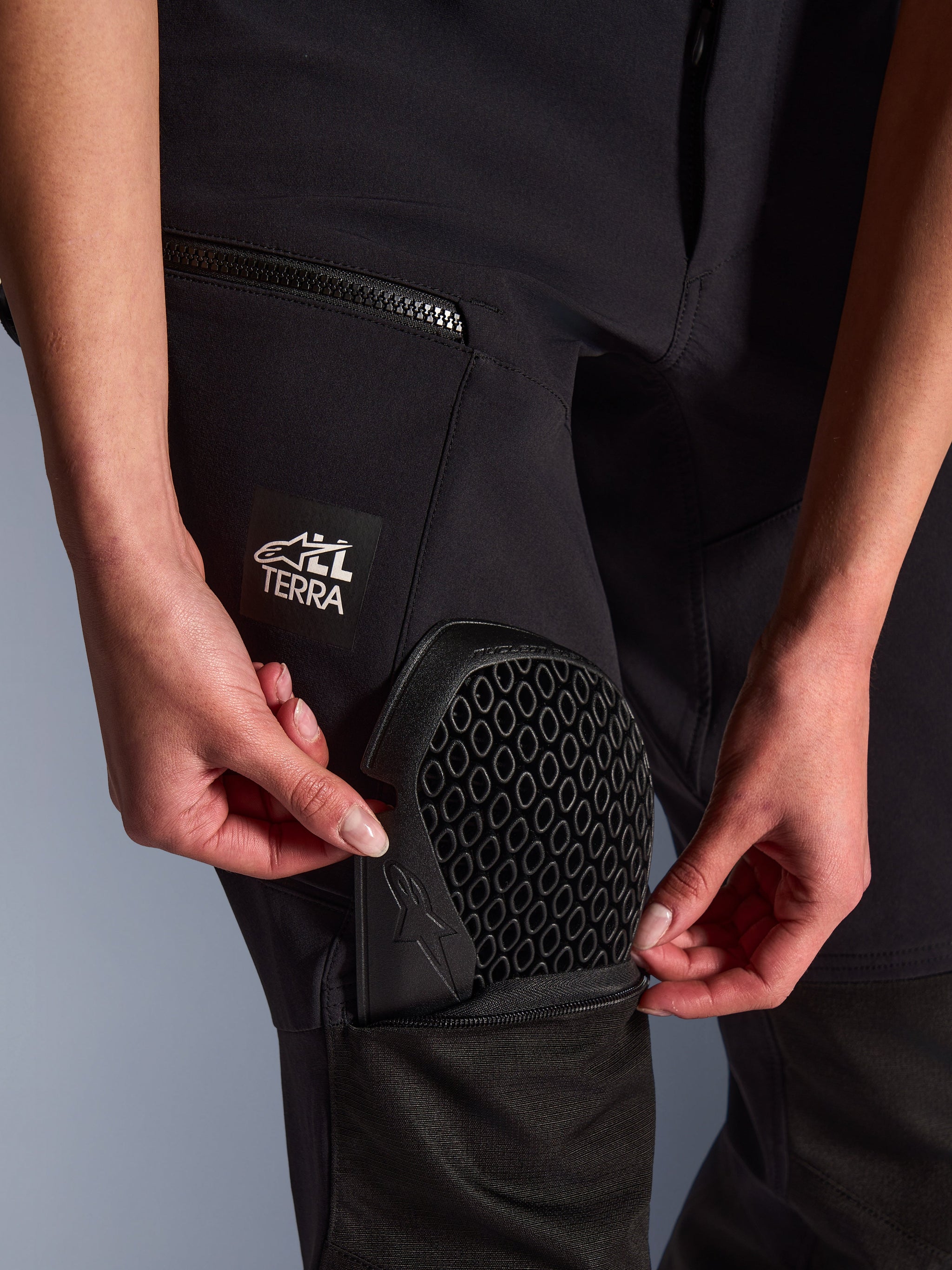 Primo piano dei pantaloni Alpinestars Stella Flex-AST Explorer neri, mostra l'inserimento della protezione per le ginocchia Nucleon Flex Plus nella tasca esterna, dettaglio della protezione con motivo a nido d'ape, marchio "ALL TERRA" sulla coscia, abbigliamento tecnico adventure da donna