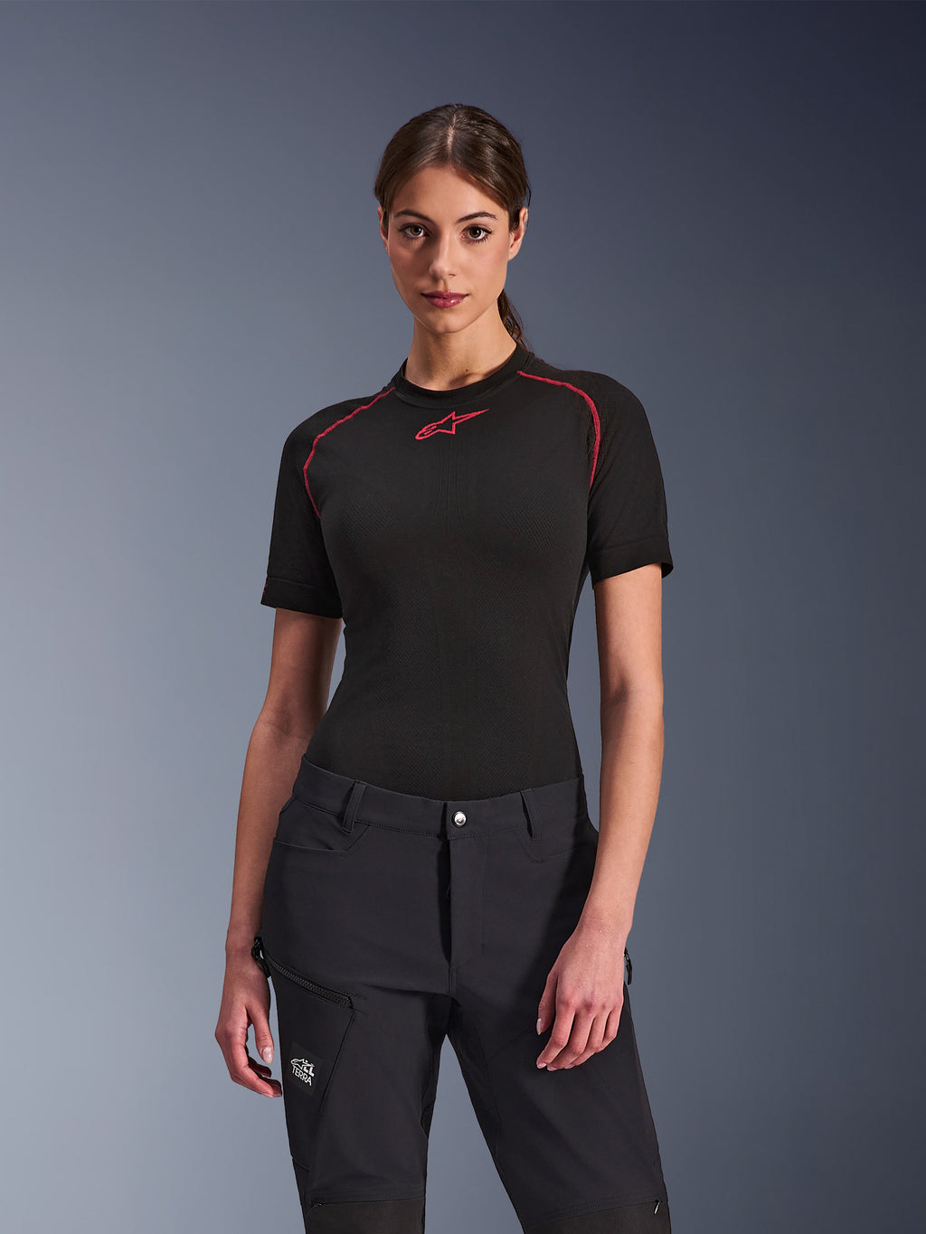 Donna che indossa i pantaloni Alpinestars Stella Flex-AST Explorer neri, abbinati a un base layer nero a maniche corte con accenti rossi, abbigliamento da guida adventure con tasche cargo e marchio All Terra