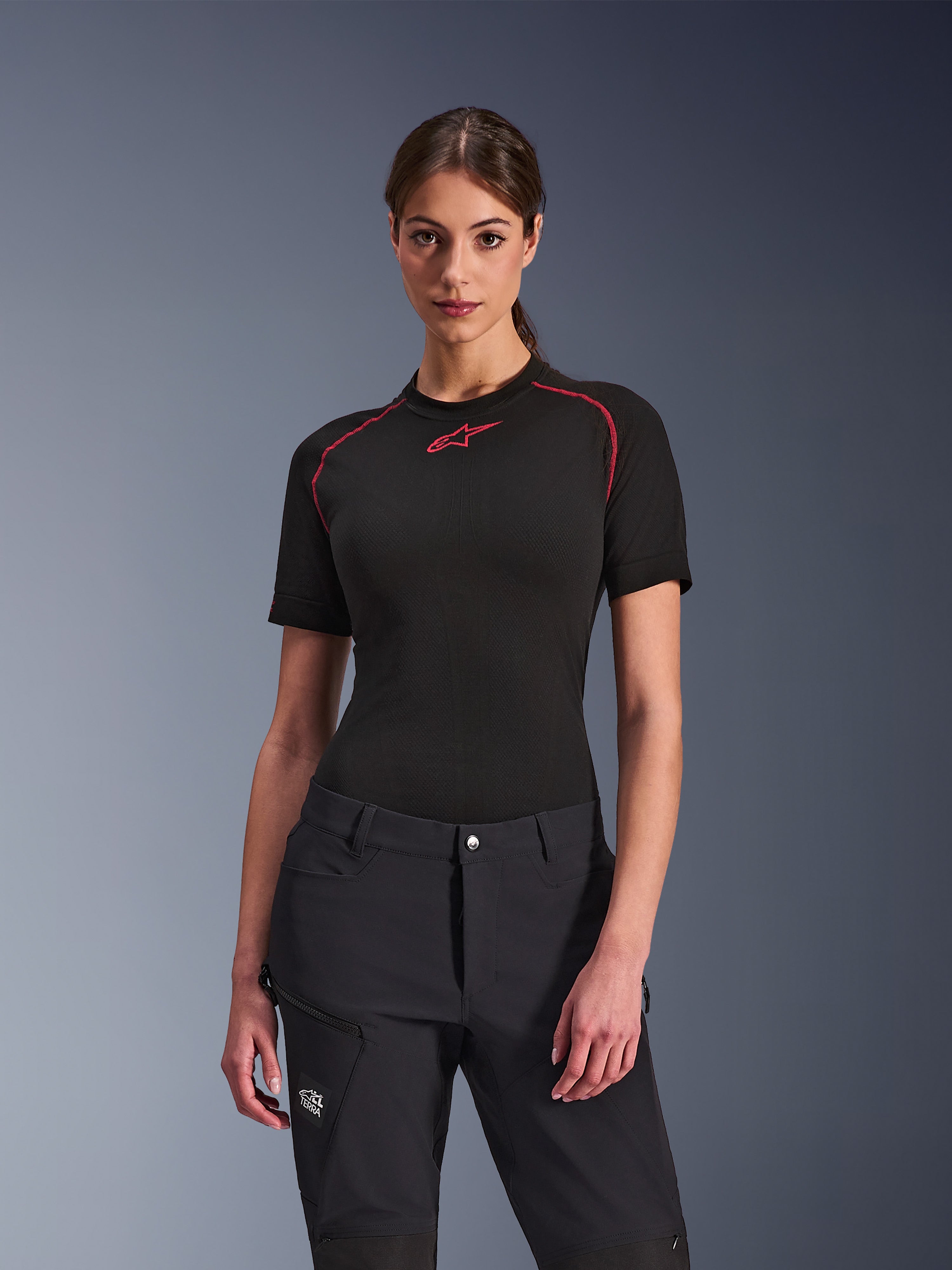 Donna che indossa i pantaloni Alpinestars Stella Flex-AST Explorer neri, abbinati a un base layer nero a maniche corte con accenti rossi, abbigliamento da guida adventure con tasche cargo e marchio All Terra