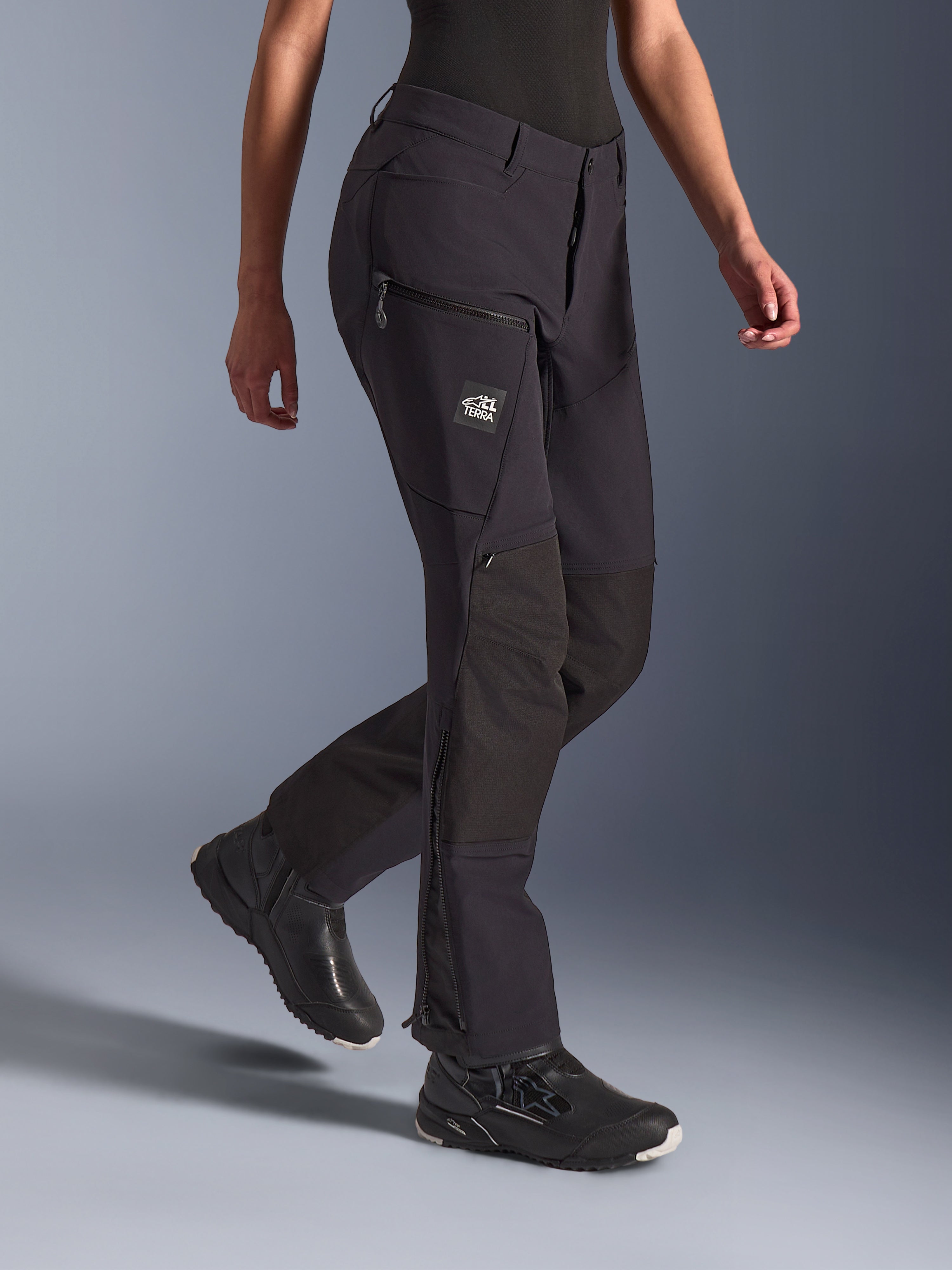 Alpinestars Pantaloni Stella Flex-AST Explorer, nero, pantaloni da moto adventure, con costruzione in tessuto elasticizzato e rinforzi in ripstop sulle ginocchia, tasche cargo con cerniera e logo TERRA, e cerniere sul fondo gamba, indossati con calzature da moto nere