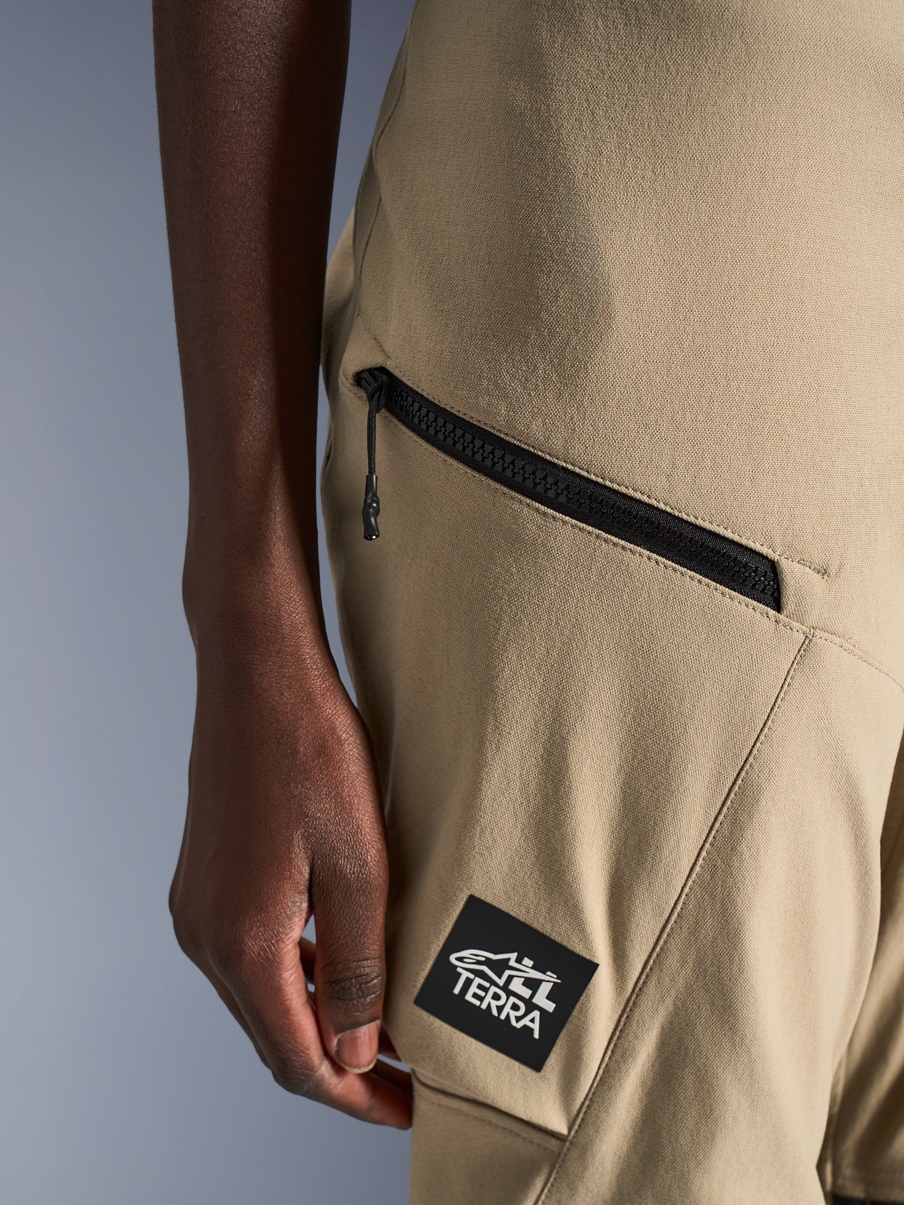 Alpinestars Stella Flex-AST Explorer Pants, pantaloni da moto da donna, sabbia, dettaglio ravvicinato della tasca cargo con cerniera e patch nera con logo ALL TERRA, costruzione in tessuto ripstop resistente per l'adventure touring