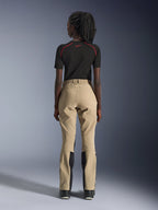 Pantaloni Alpinestars Woman Stella Flex-AST Explorer in Sand, vista posteriore su modella, abbinati a un base layer nero a maniche corte e stivali neri, con pannelli rinforzati sulla seduta e costruzione ergonomica in tessuto per adventure touring
