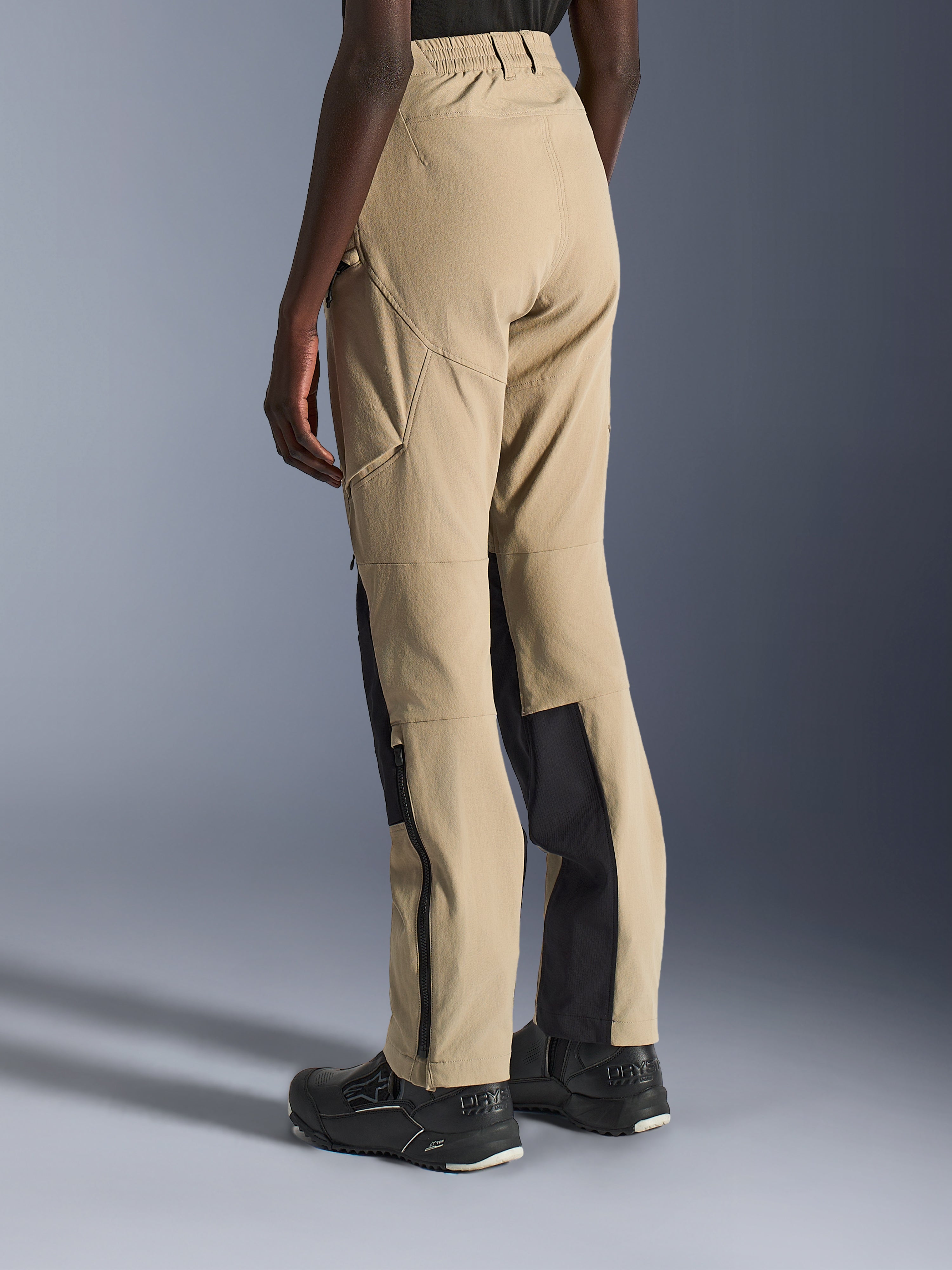 Alpinestars Pantaloni Stella Flex-AST Explorer da donna, colore sabbia e nero, vista posteriore e laterale su modella, costruzione leggera in ripstop, pannelli di rinforzo neri sull'interno polpaccio, tasche cargo con cerniera e cerniere a fondo gamba per guida adventure