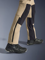 Alpinestars Pantaloni Stella Flex-AST Explorer da donna, pantaloni da moto adventure, sabbia e nero, vista ravvicinata della parte inferiore delle gambe e delle caviglie con una lunga cerniera laterale e pannelli di rinforzo neri, indossati con scarpe da moto Alpinestars nere.